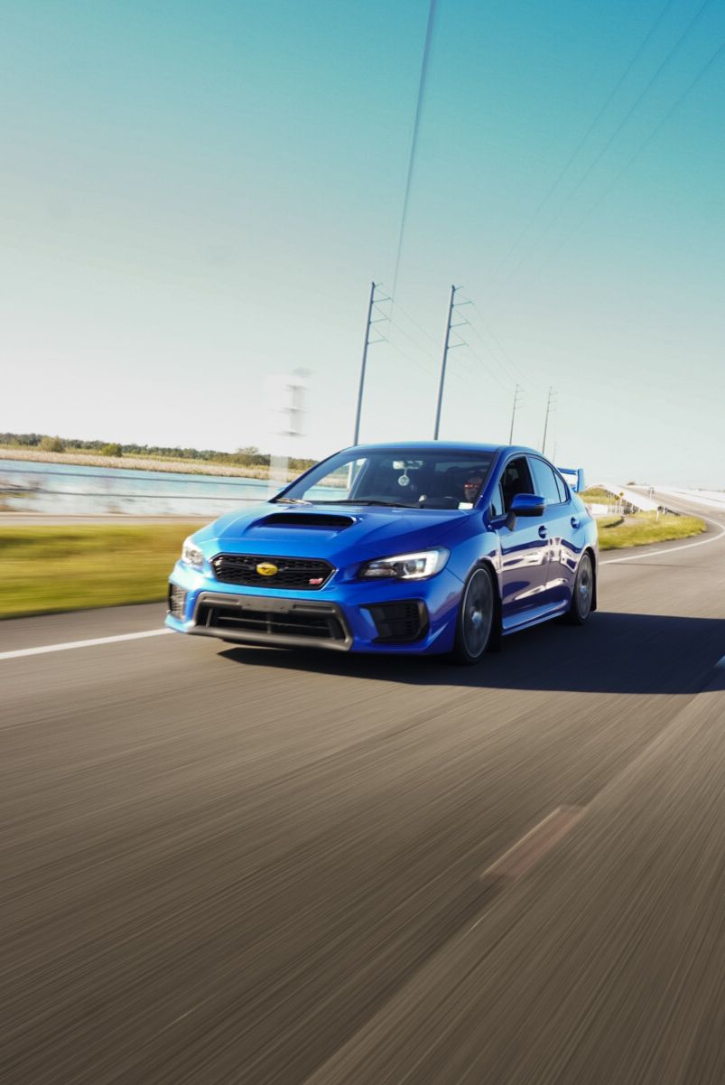 Blue Subaru WRX STI sedan speeding on open road under clear blue sky with blur.