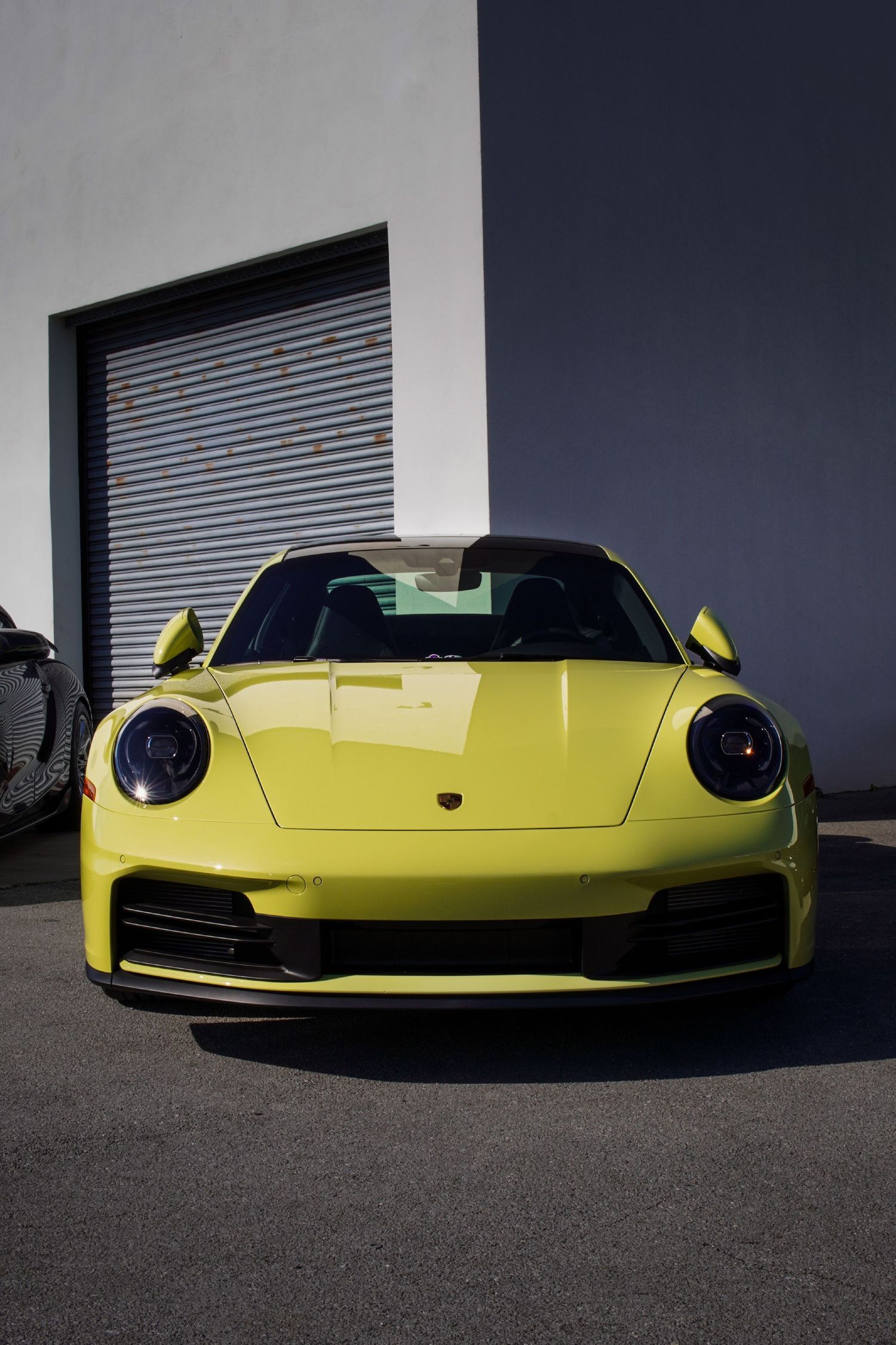 Bright yellow Porsche 911 sports car parked in front of garage door in sunlight.