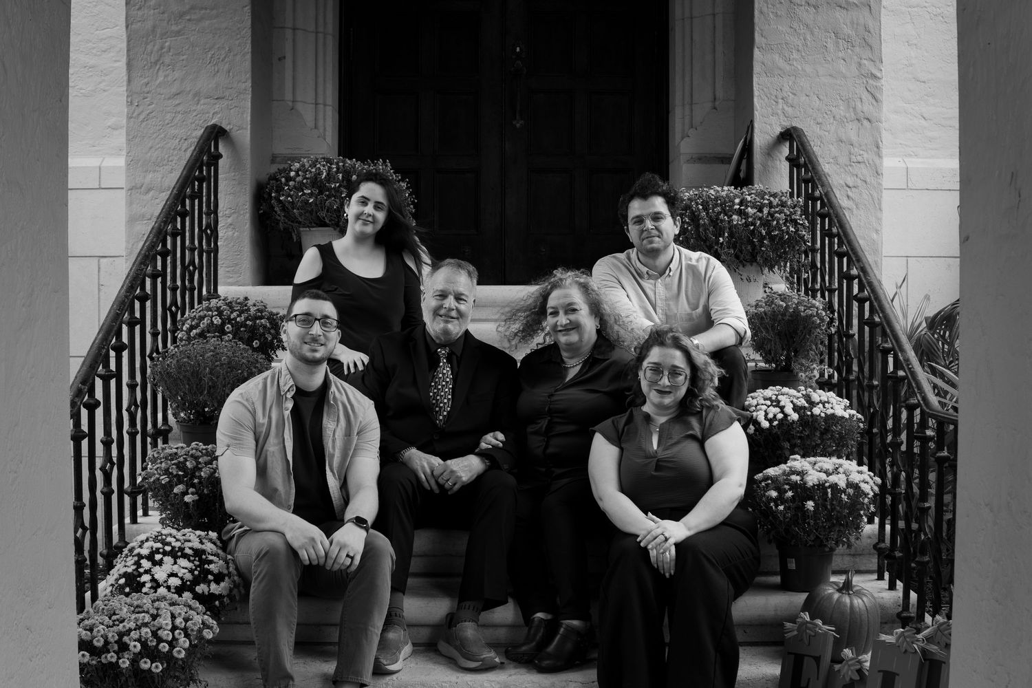 Black and white family portrait of six people posed on decorative front steps.