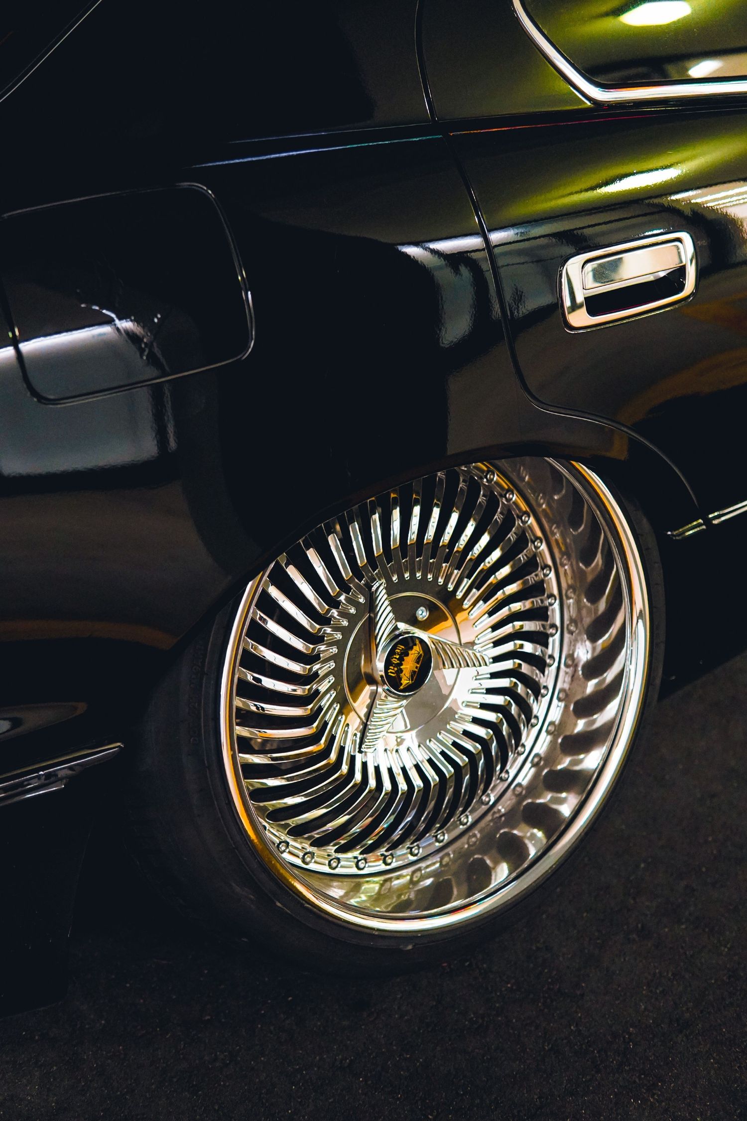 Close-up of chrome wire spinner wheel on lowrider black classic car in dark setting.