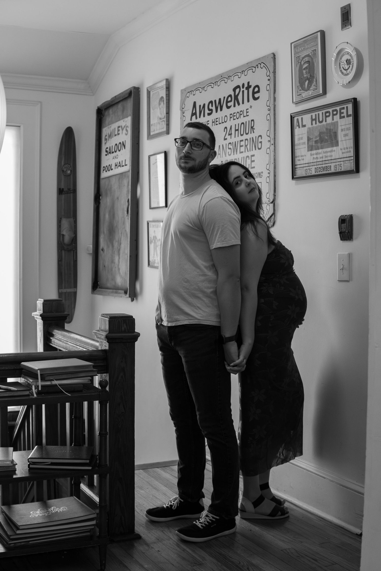 Black and white photo of couple holding hands indoors with vintage wall art in background.