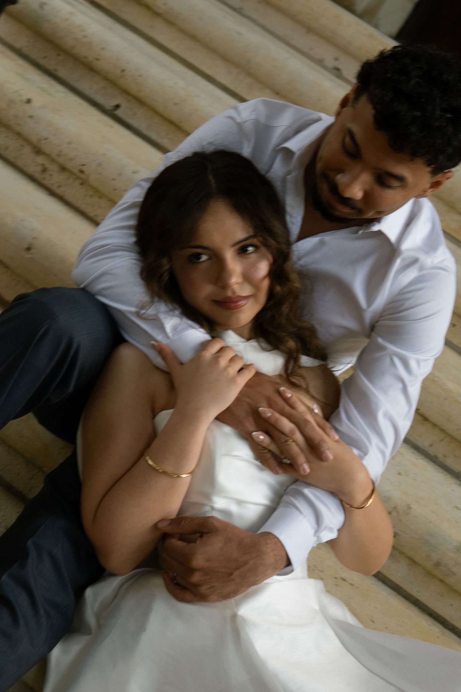 Couple embracing on steps, woman in white dress leaning back against man in white shirt, smiling.