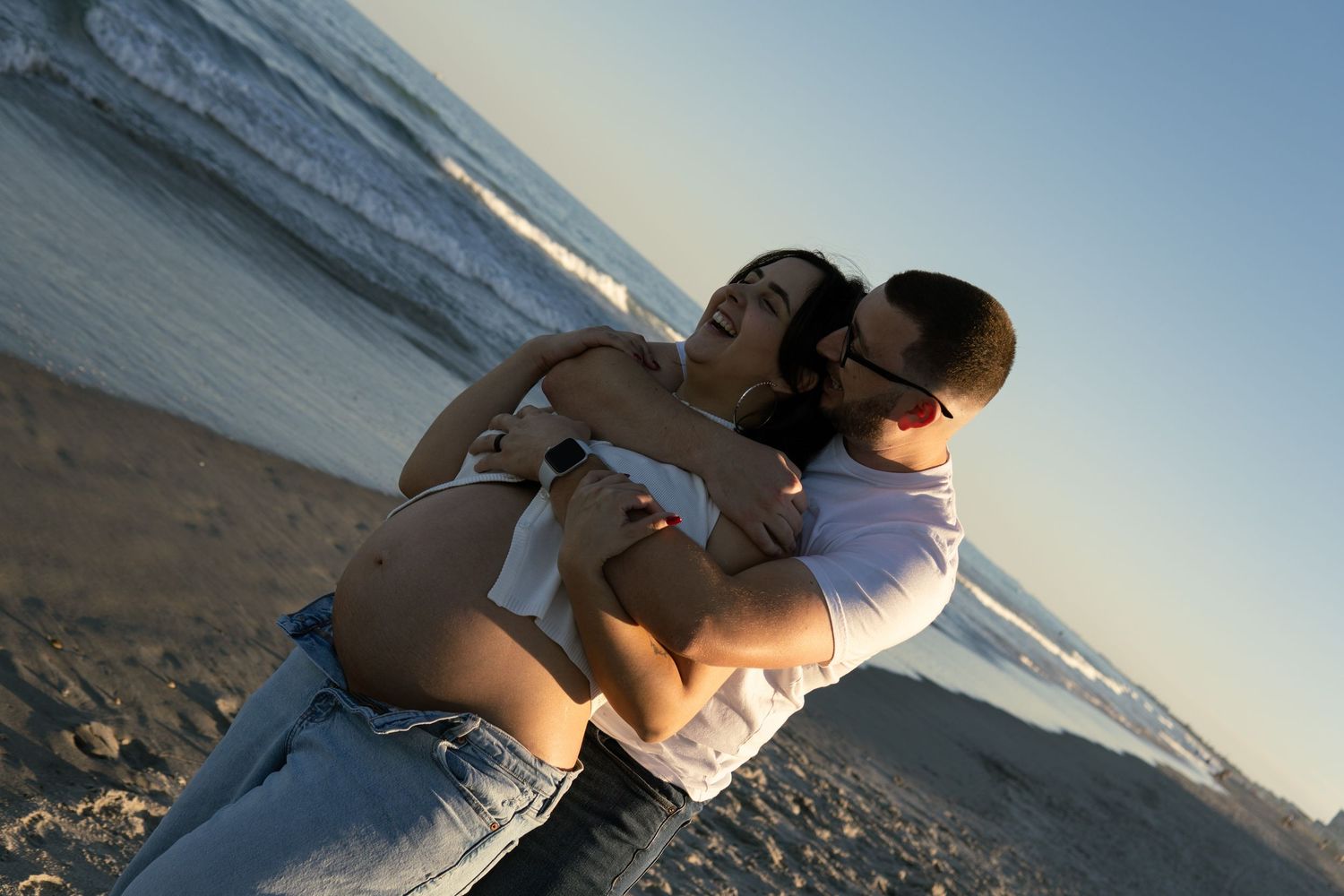 A couple shares a tender embrace on a sandy beach during a warm golden sunset.