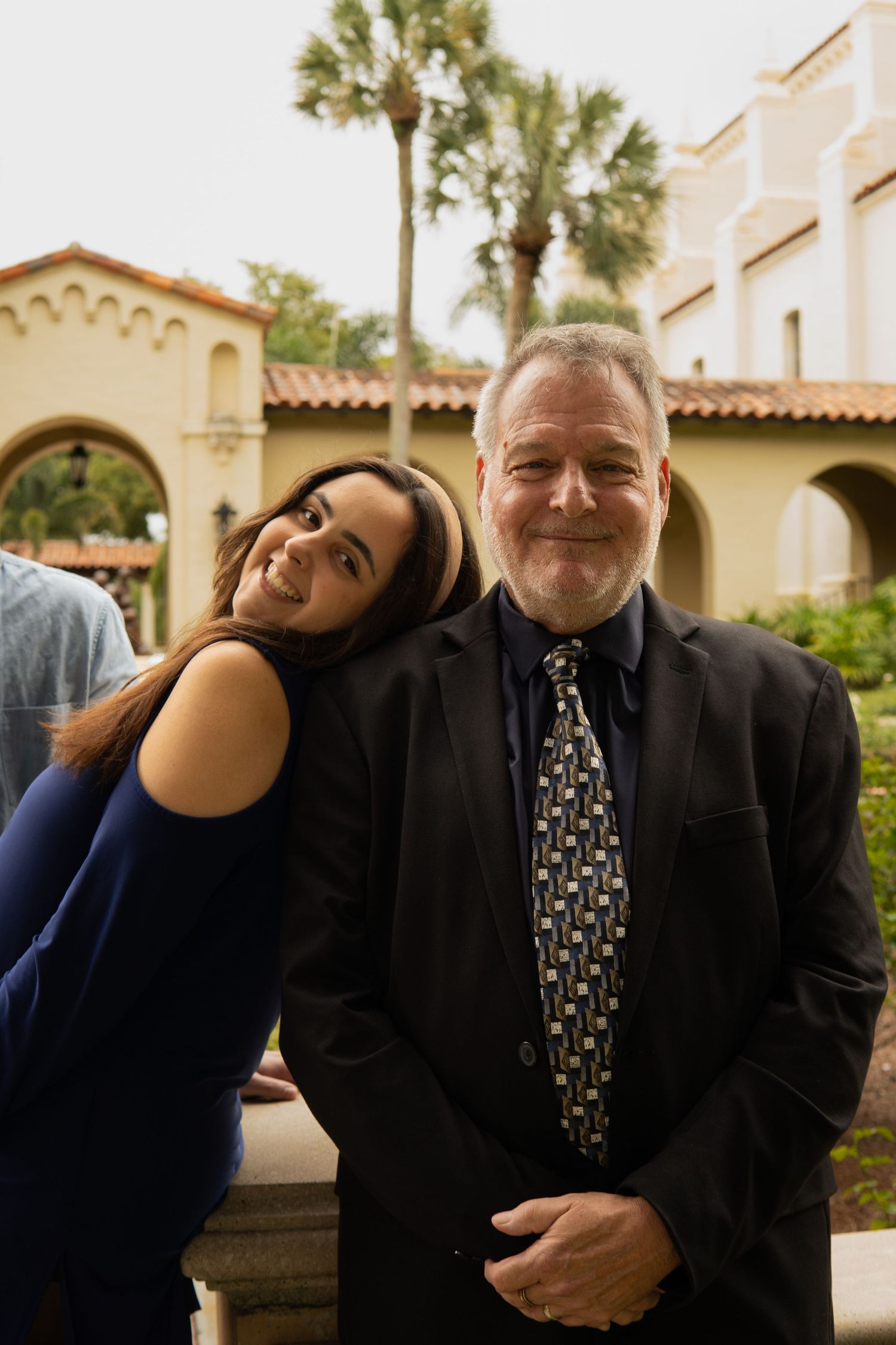Young woman and older man in suit smiling together outdoors near palm trees.
