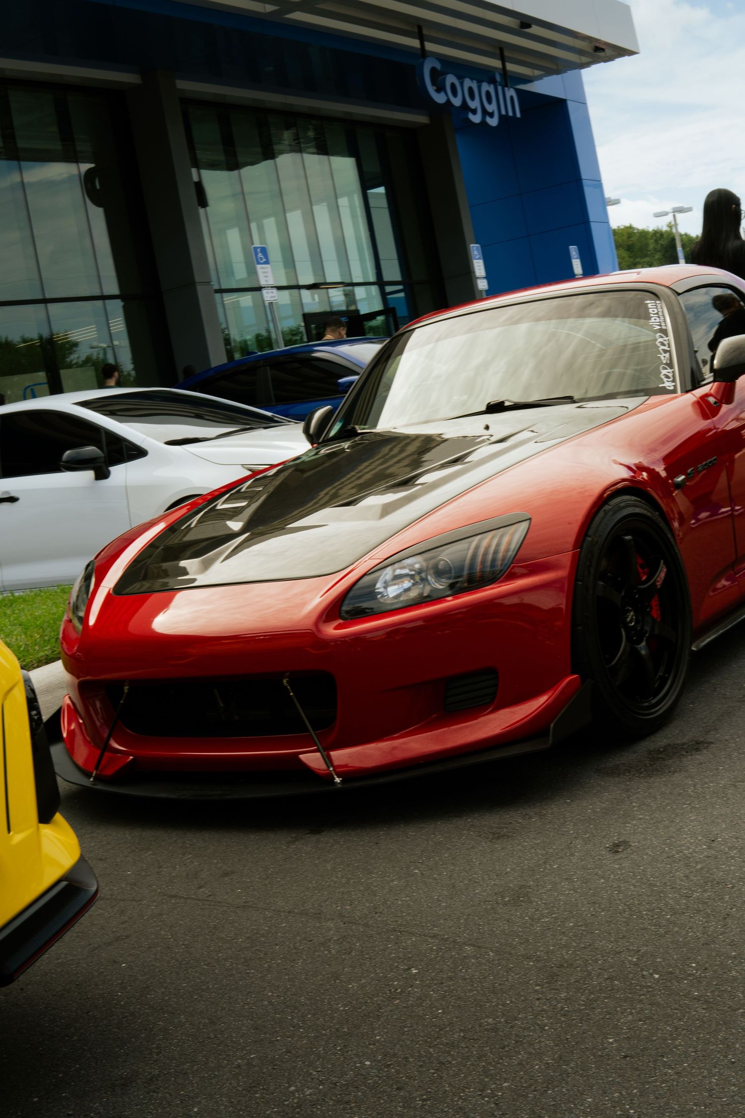 Modified red Honda S2000 with carbon fiber hood parked at a Coggin dealership car meet.