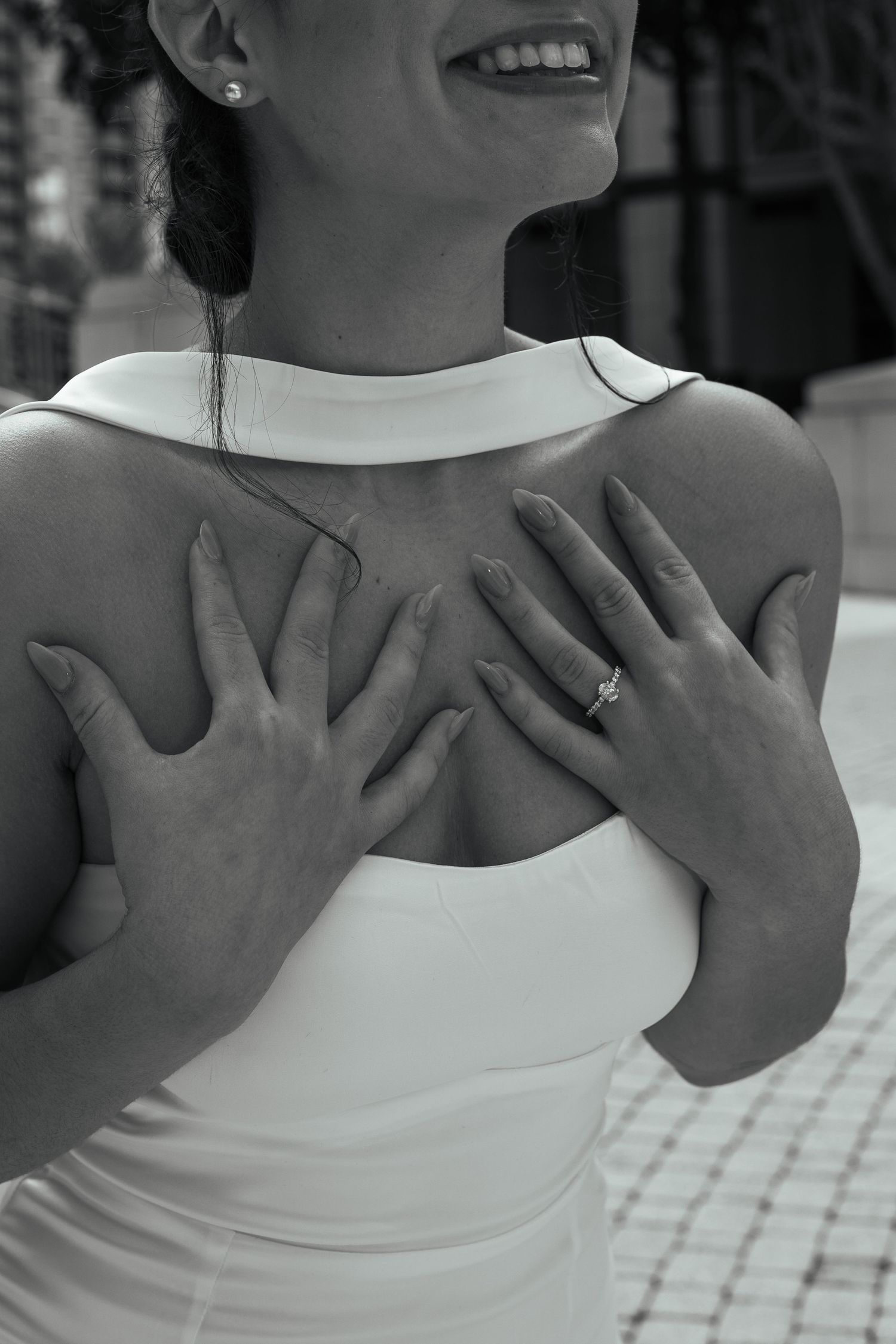 Black and white close-up of bride in white dress with hands crossed over chest showing diamond engagement ring.