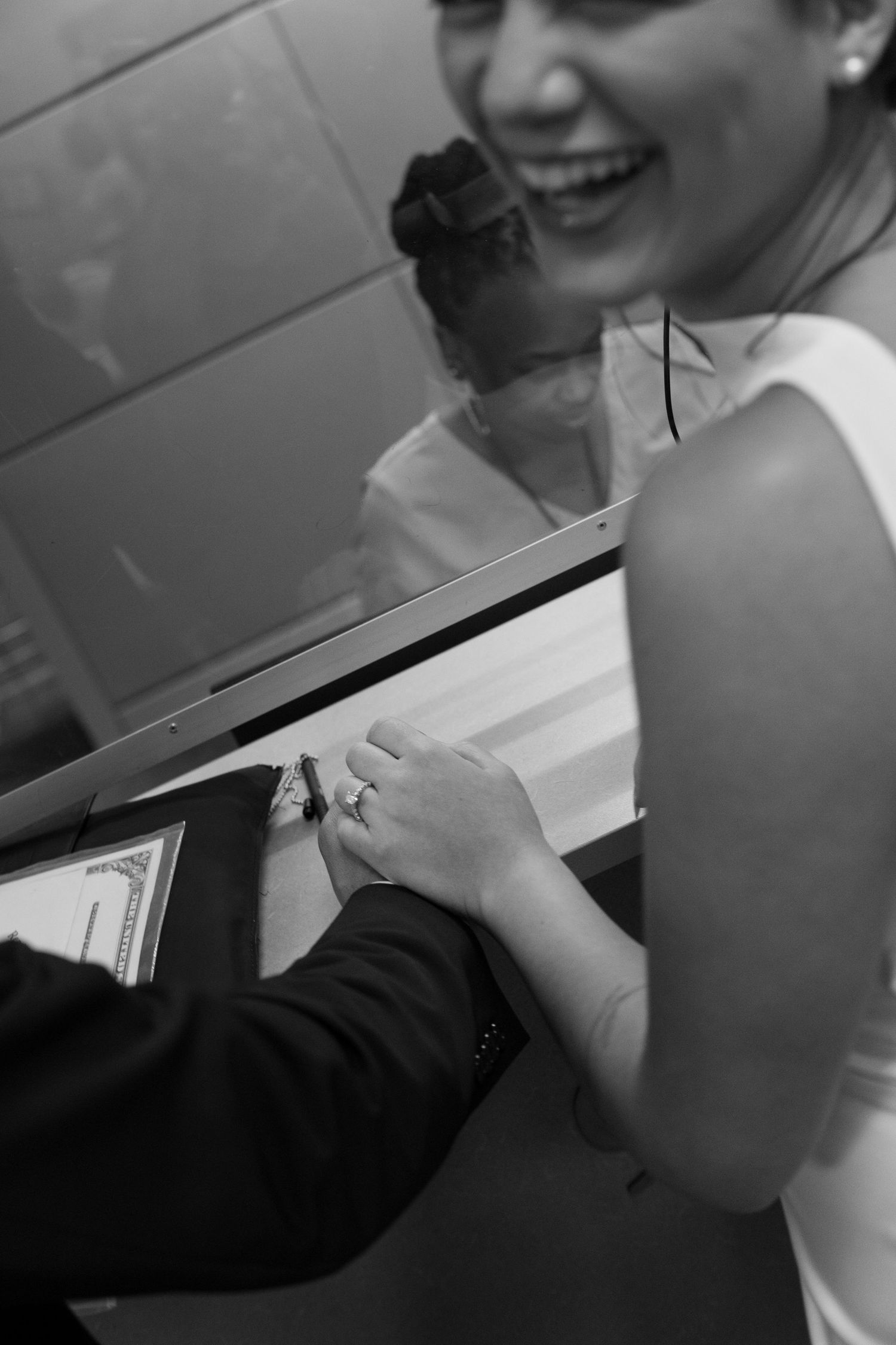 Black and white photo of smiling bride signing marriage documents at a courthouse counter.