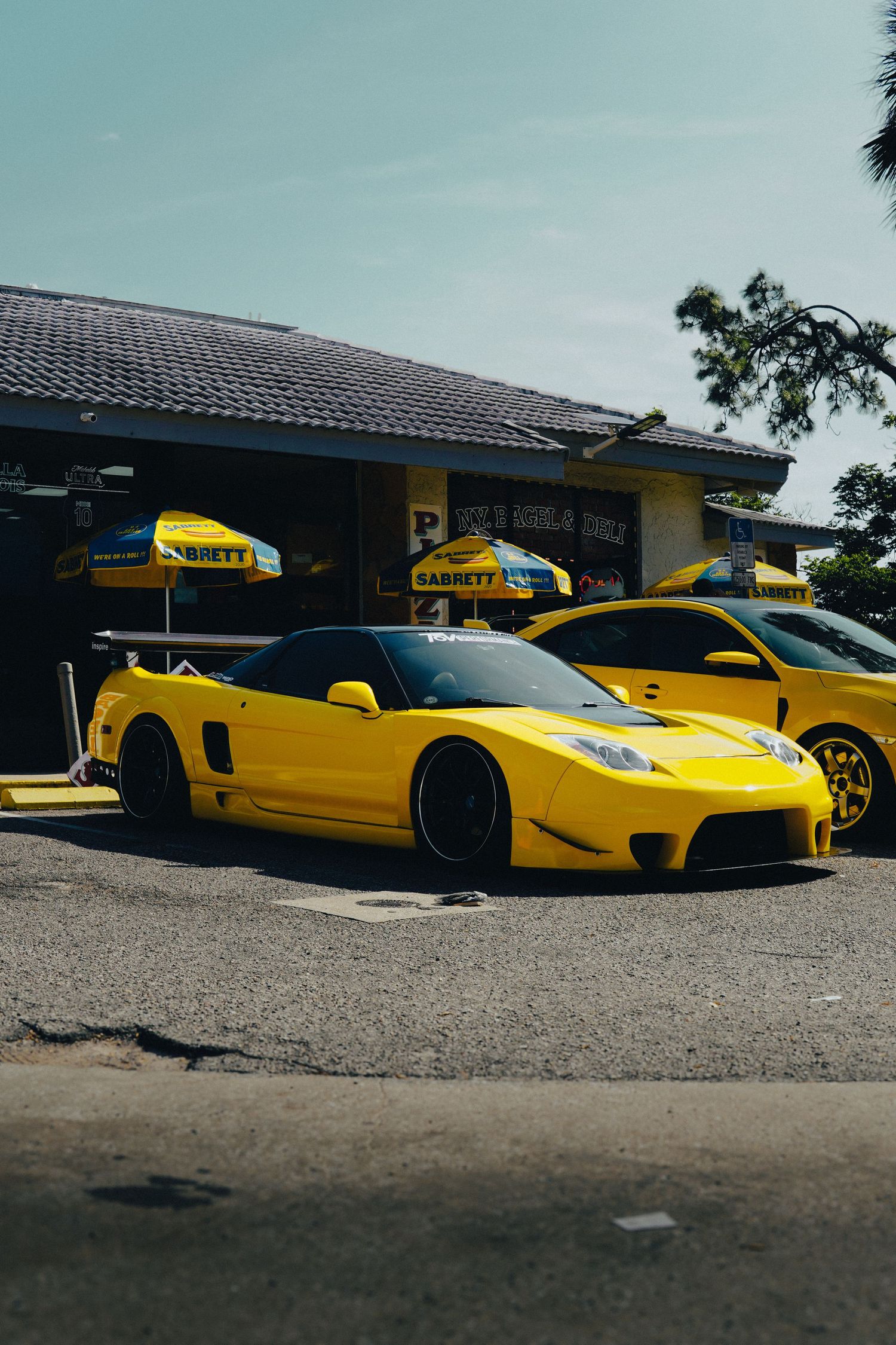 Modified yellow Honda NSX sports car parked outside a shop on a sunny day.