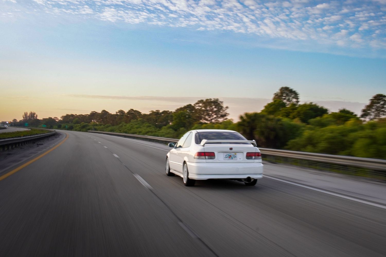 White Toyota Chaser speeding down a highway at sunset with motion blur background.