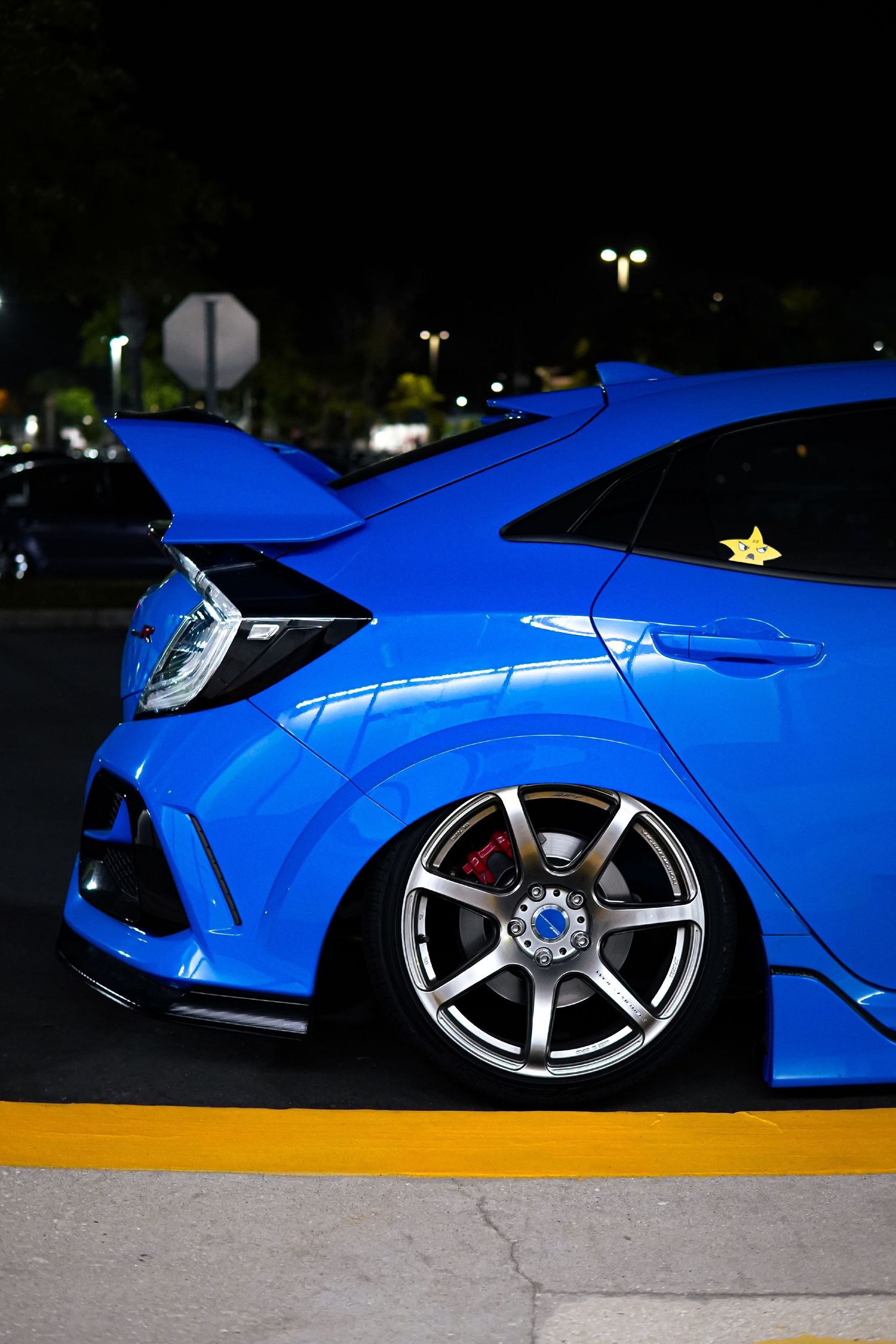 Blue Honda Civic Type R with large spoiler and aftermarket wheels at night car meet.