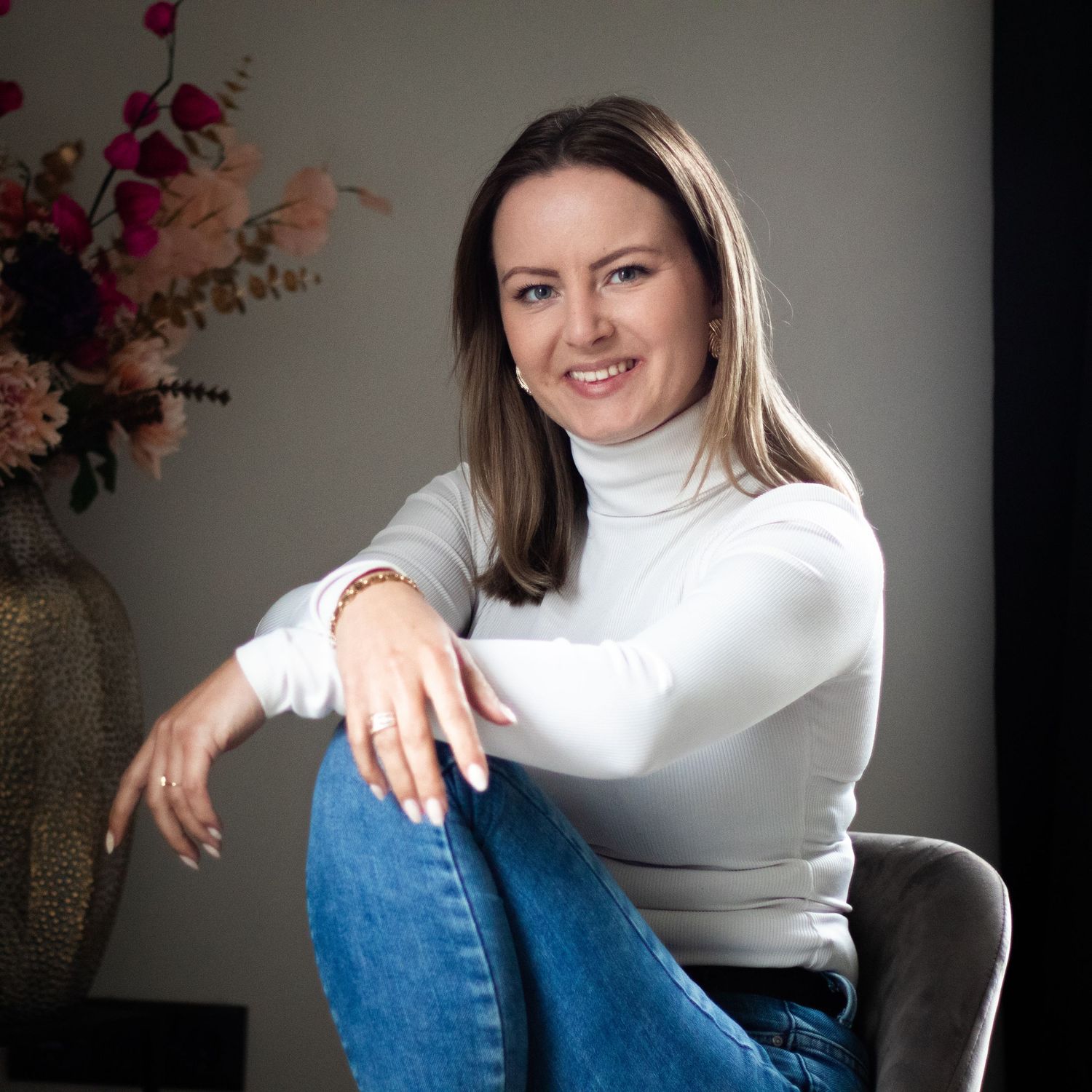 Woman in white turtleneck and jeans poses in casual portrait series against neutral background.
