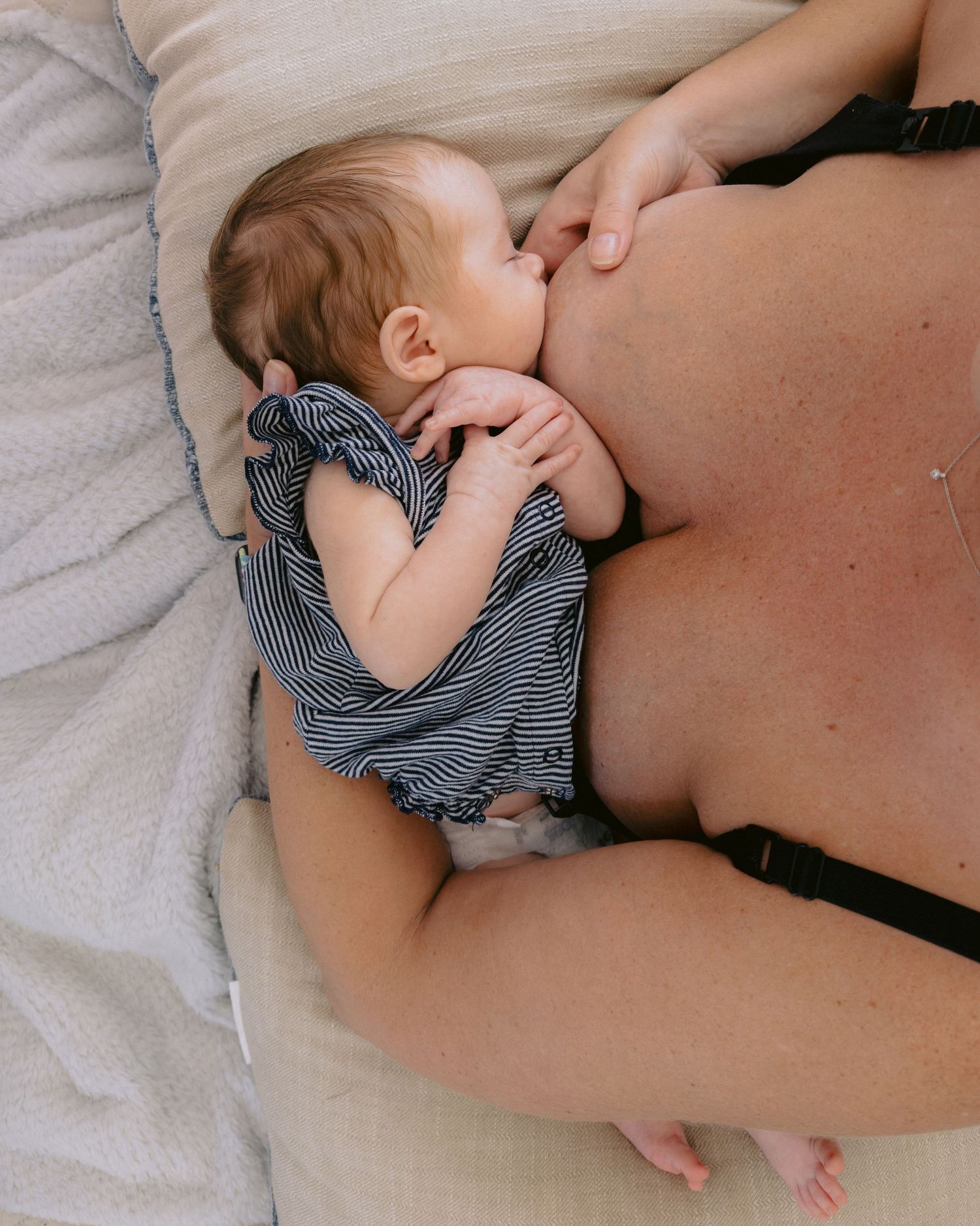 A baby in striped clothing lies nursing while resting on a pillow bed.