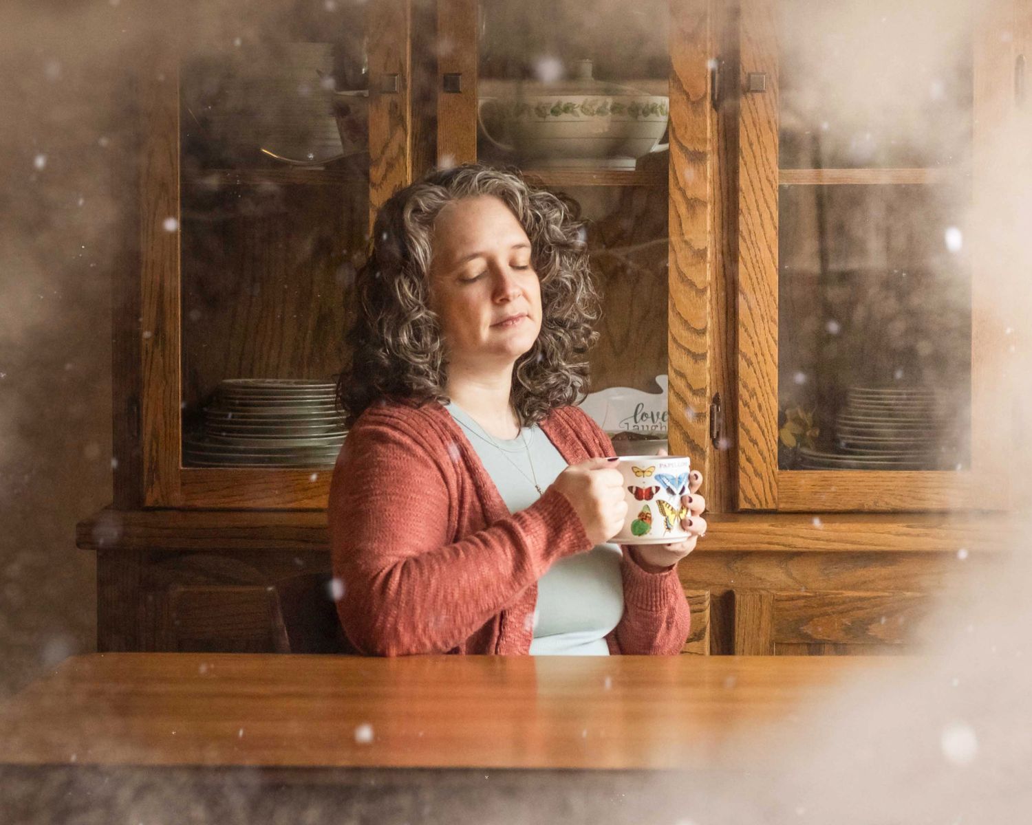 Woman sits at table with eyes closed holding a cup of tea