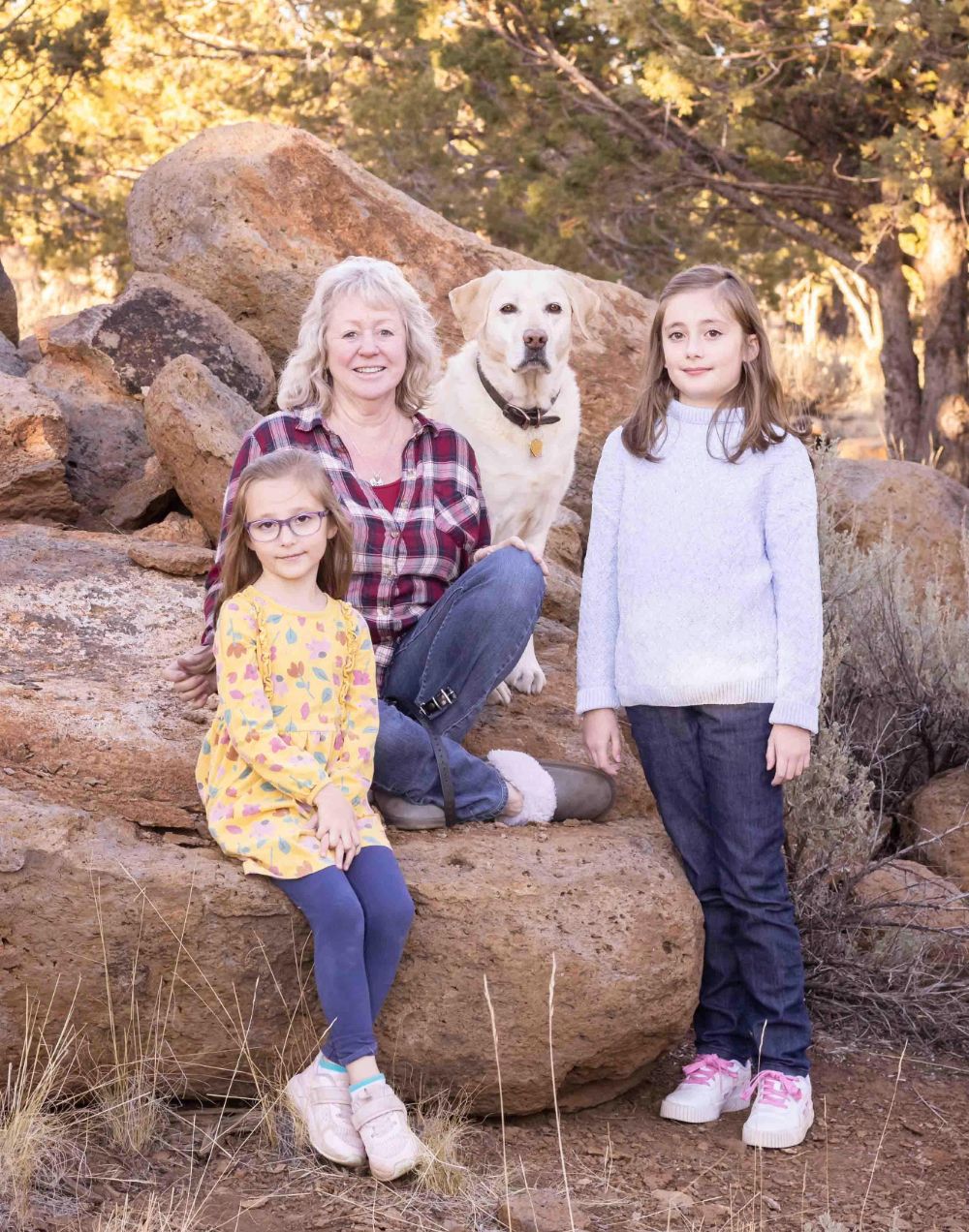 A grandma, her dog, and two grand-daughters sit on rocks outside