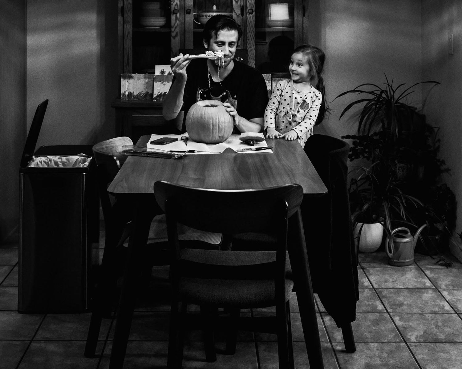 Dad carving a pumpkin at the kitchen table while his little girl watches