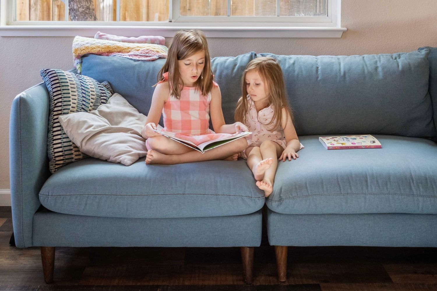 Two girls sit on a couch and read a book