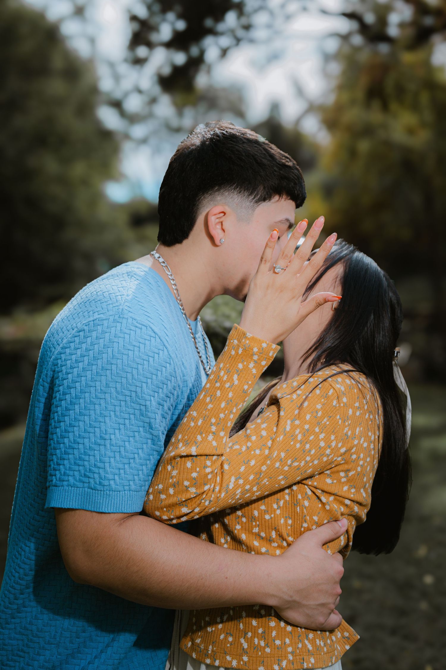 A romantic couple shares an intimate embrace outdoors, wearing coordinating blue and yellow outfits.