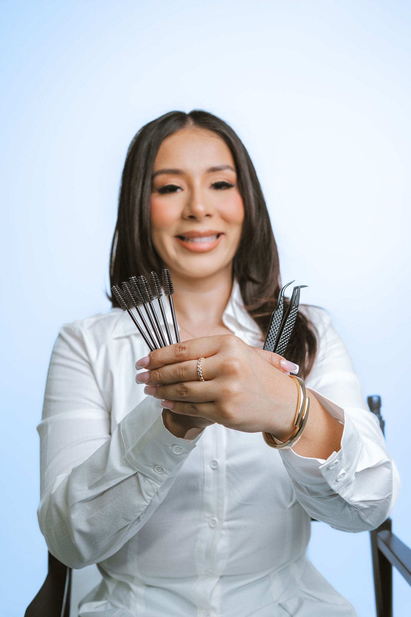 Professional in white blouse displays makeup brushes while demonstrating beauty tools against light background.
