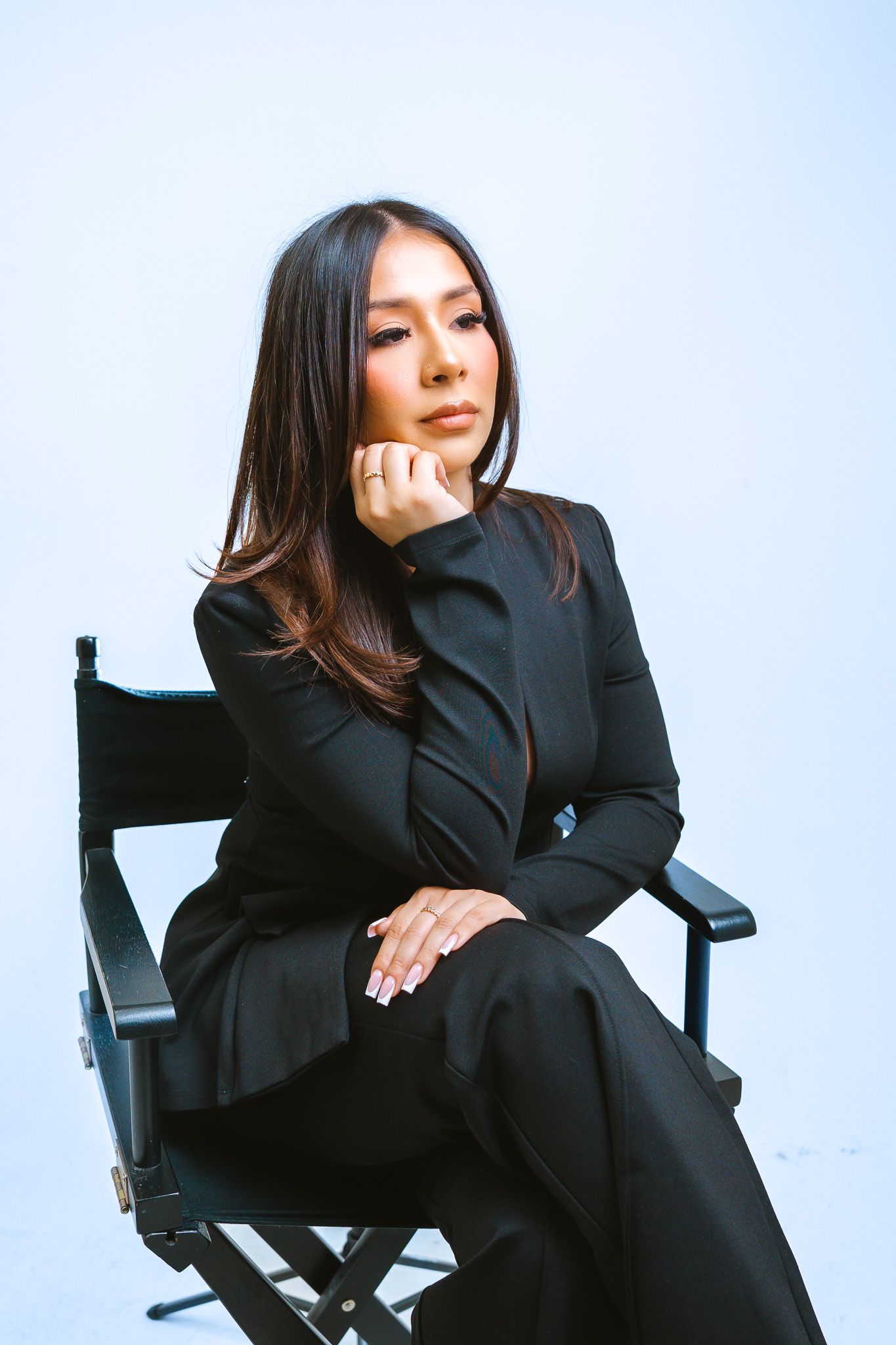 A person in a black blazer poses thoughtfully on a chair against a white background in a series of artistic shots.