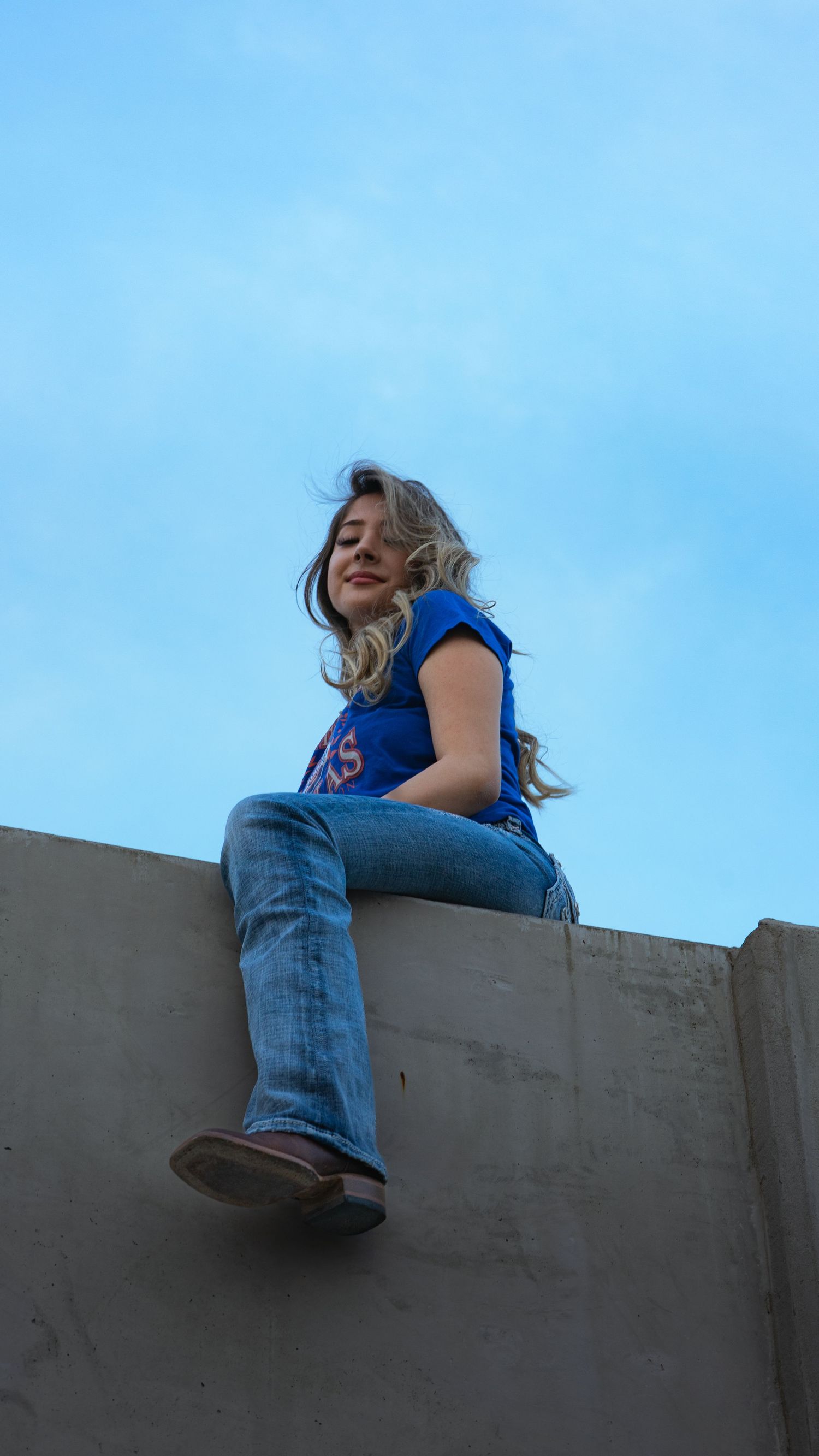 Casual rooftop pose against bright blue sky wearing denim and royal blue.