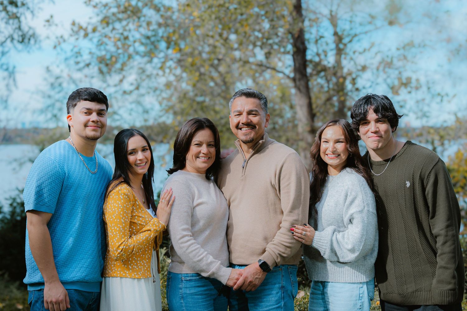 A group of people in casual attire pose together outdoors with autumn trees in the background.
