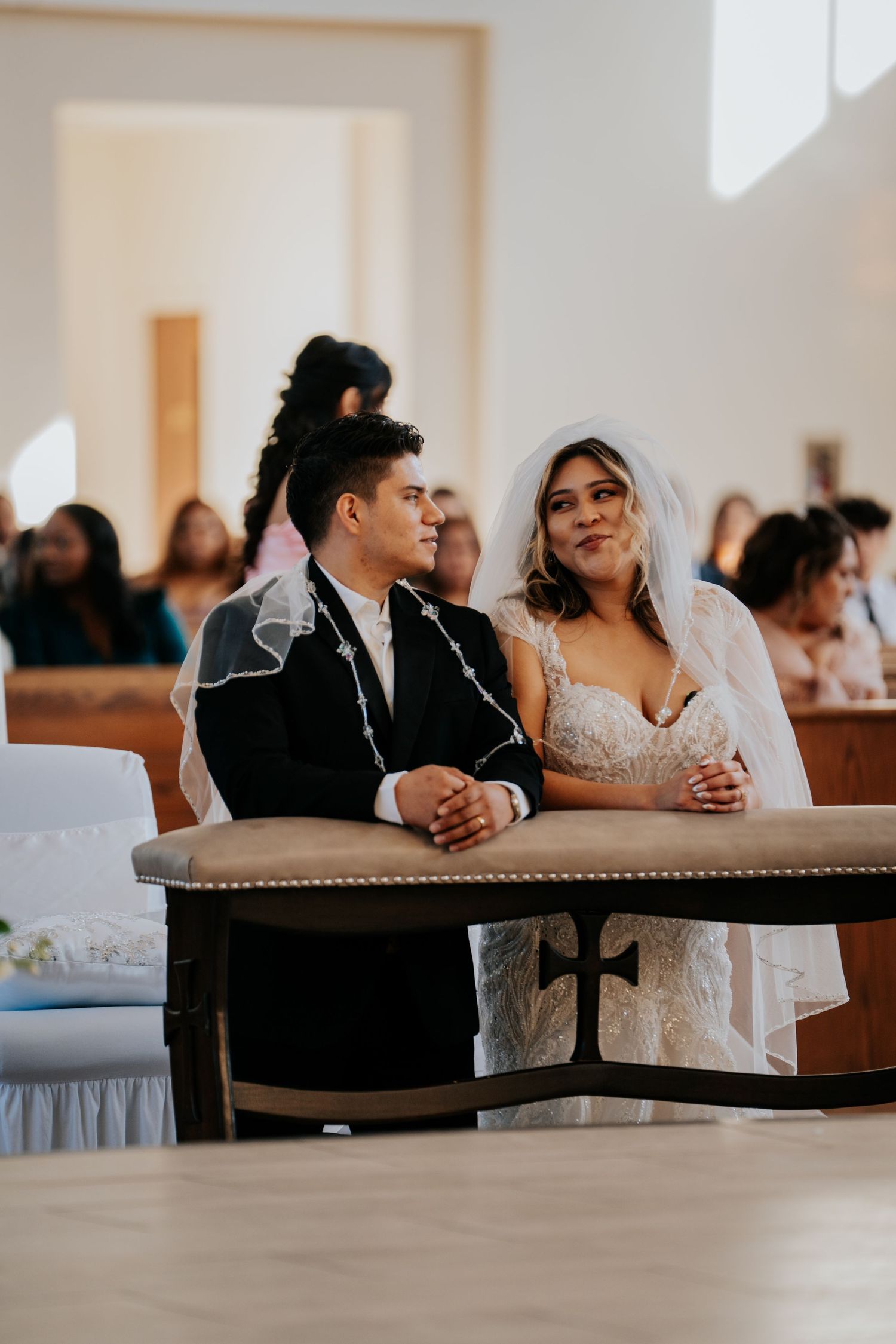 A couple shares a joyful moment during their wedding ceremony while seated at a wooden table in a church.