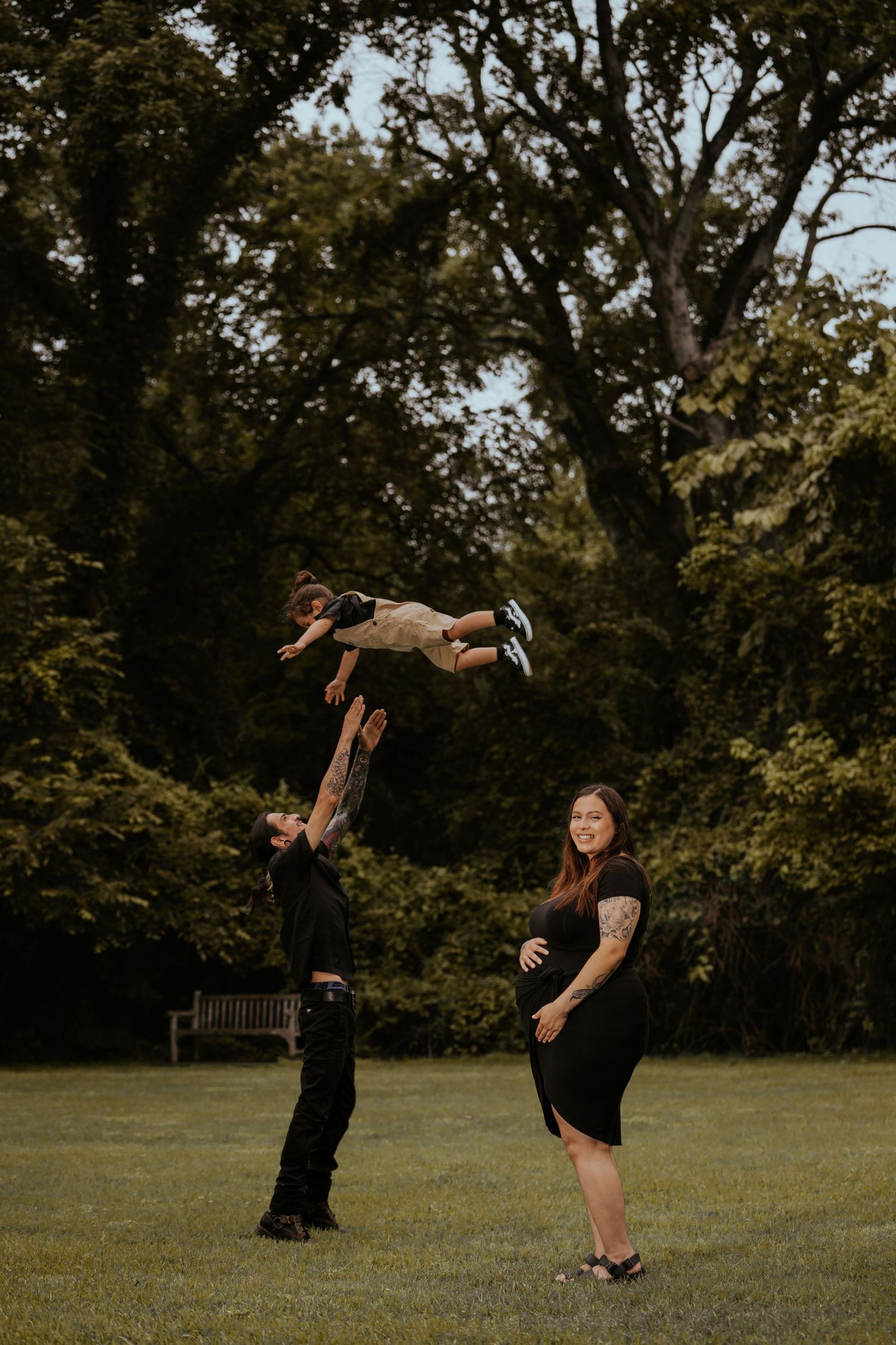 Playful family moment captured in a park with trees in the background.
