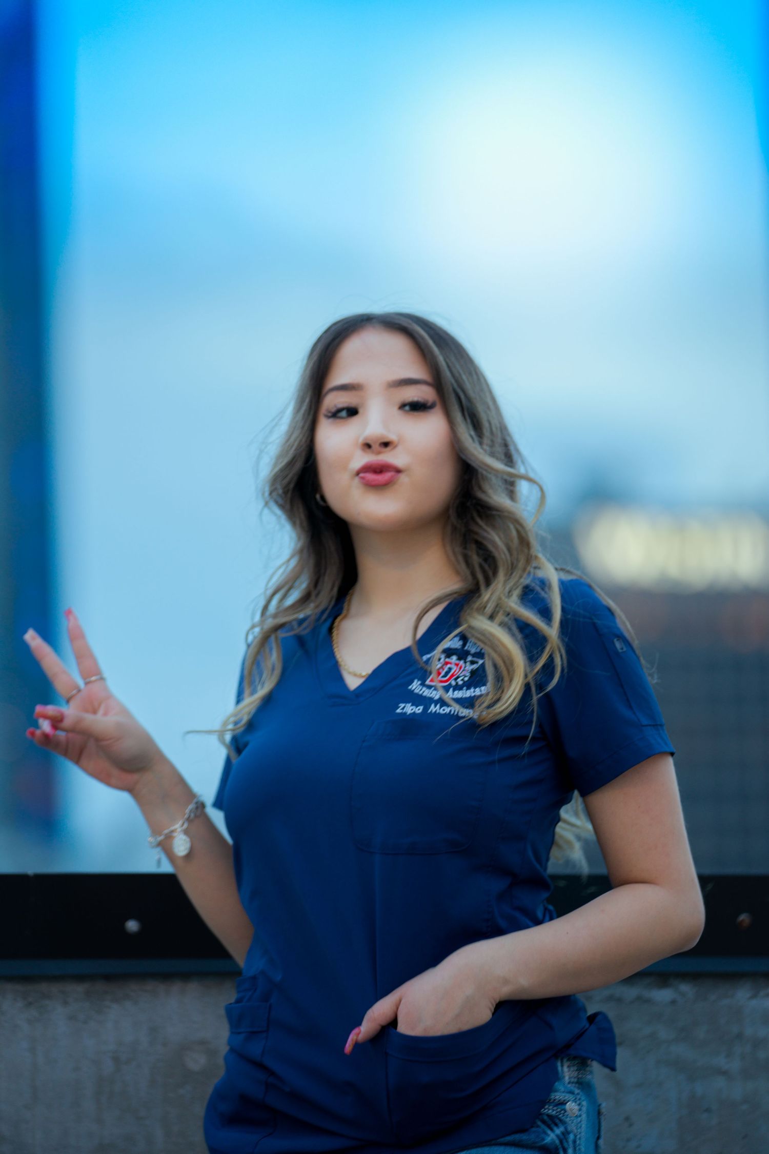 A person in a navy blue polo shirt makes a peace sign gesture against a blurred blue background.