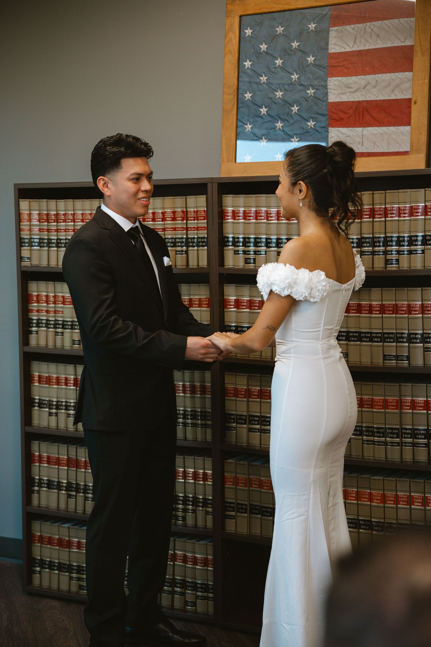 Couple exchanging vows at a courthouse wedding ceremony in front of law books and an American flag.