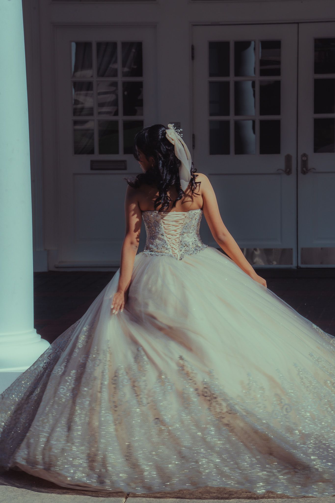 Bride in a stunning strapless ball gown with intricate beading and lace corset back, posing outdoors near elegant white doors.