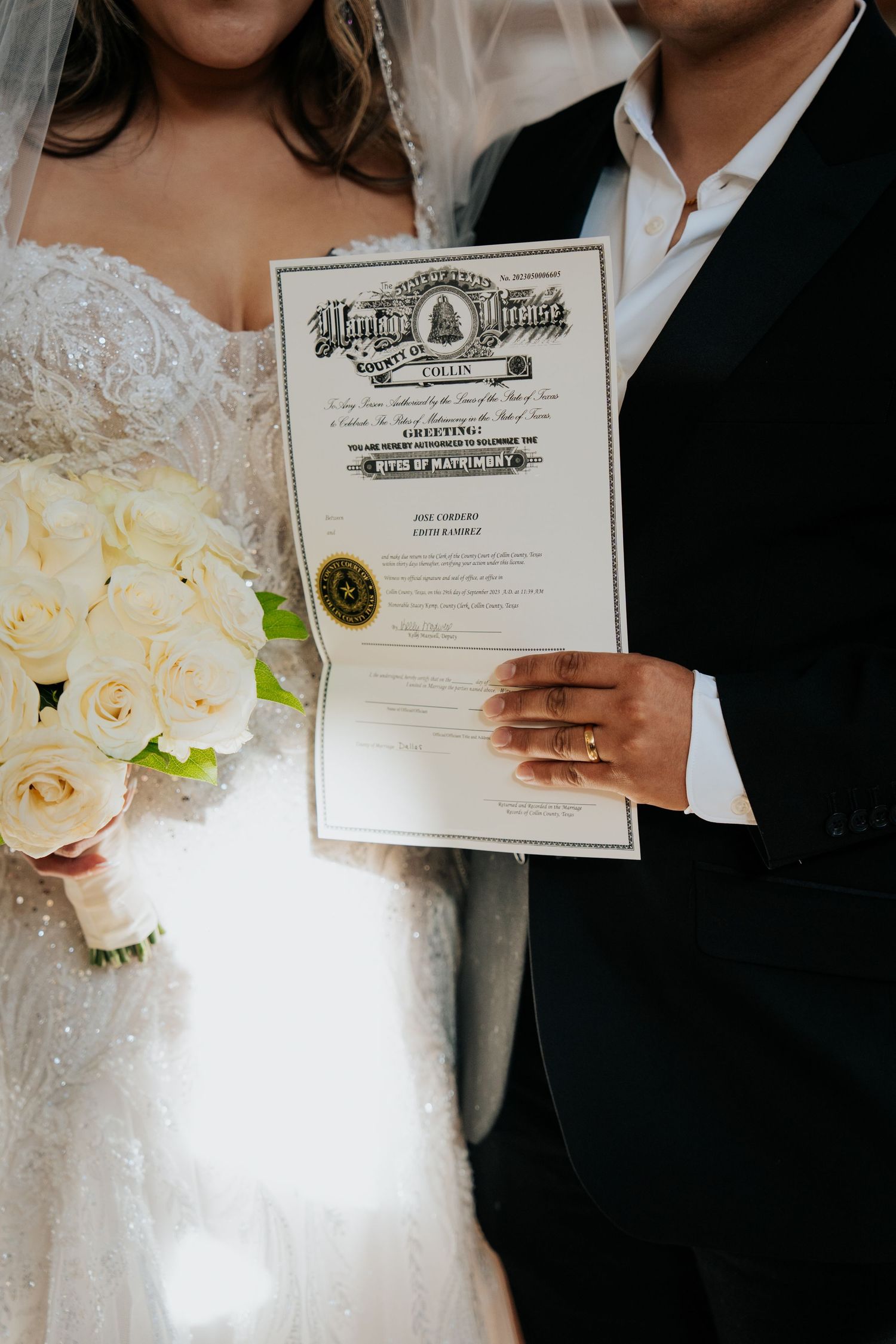 A couple holds their marriage certificate with a beautiful white rose bouquet in the foreground.