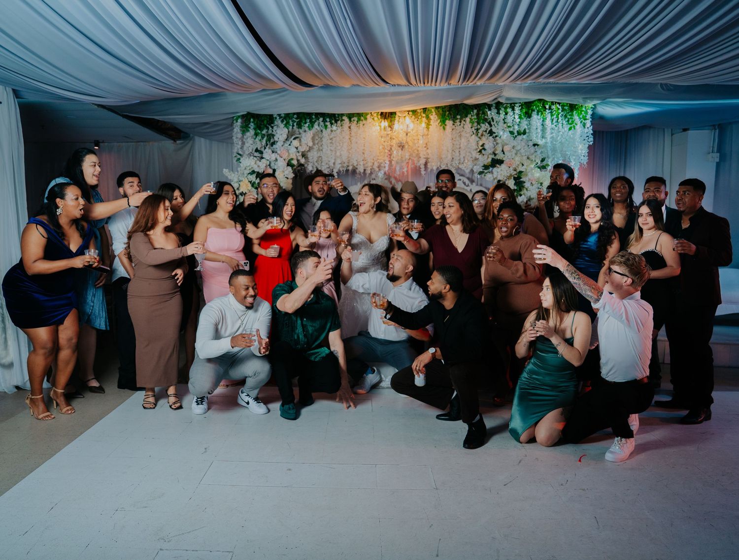 Wedding guests enjoy dancing and socializing at a reception under elegant blue draped ceiling decor.