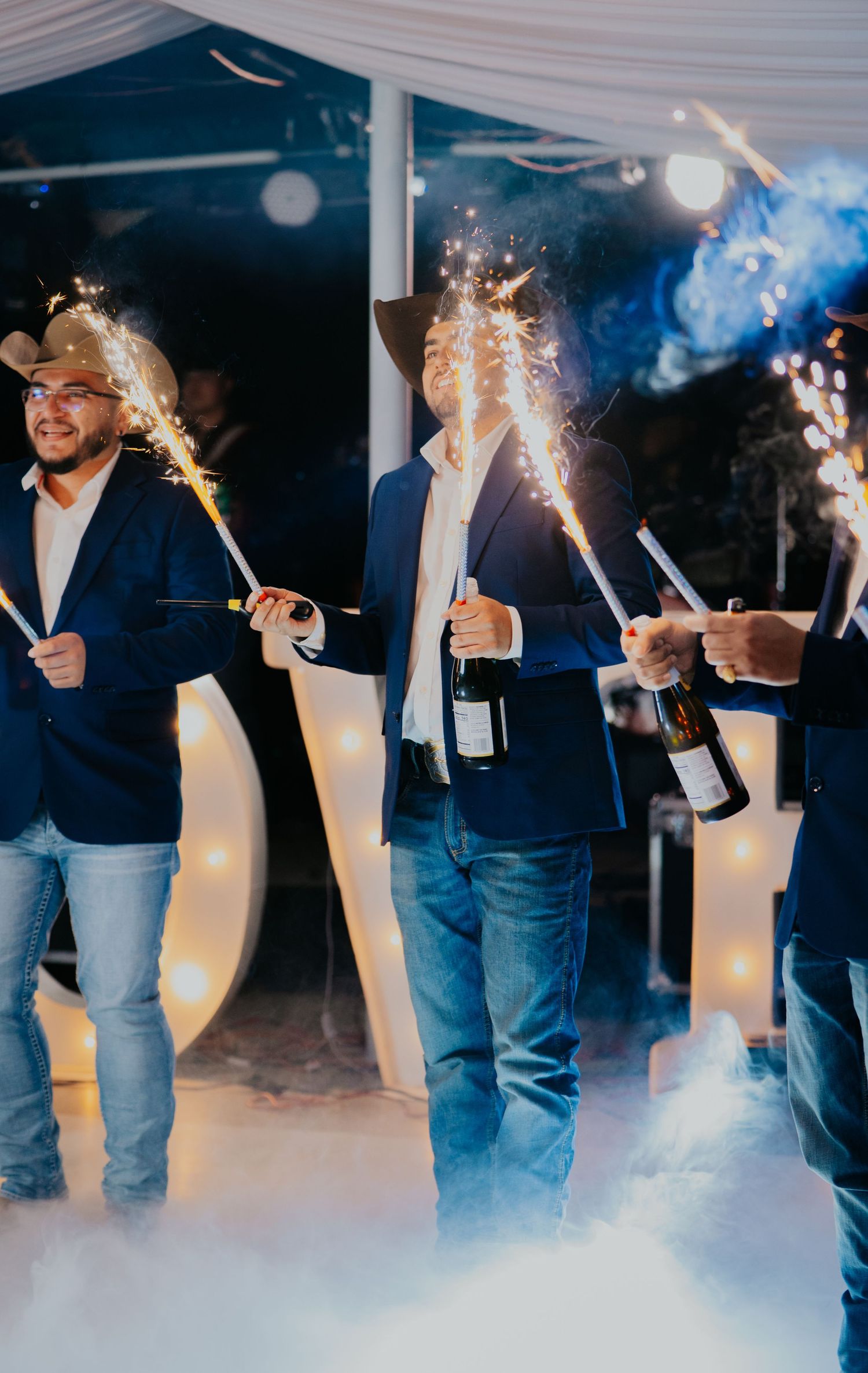 People holding sparklers create a festive atmosphere at an indoor celebration with glowing lights and smoke effects.