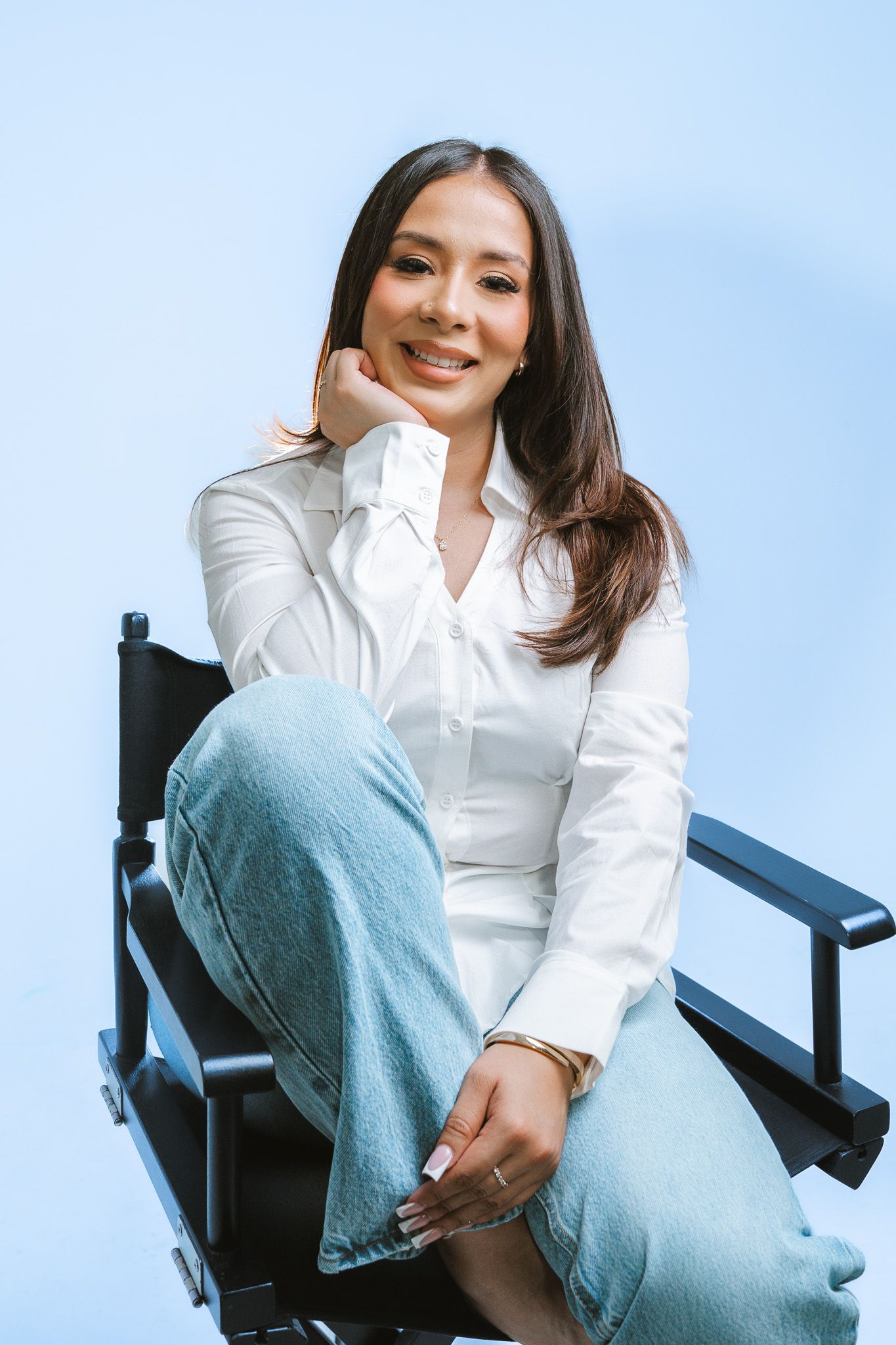 Casual fashion photography featuring a model in white shirt and jeans relaxing on a director's chair.