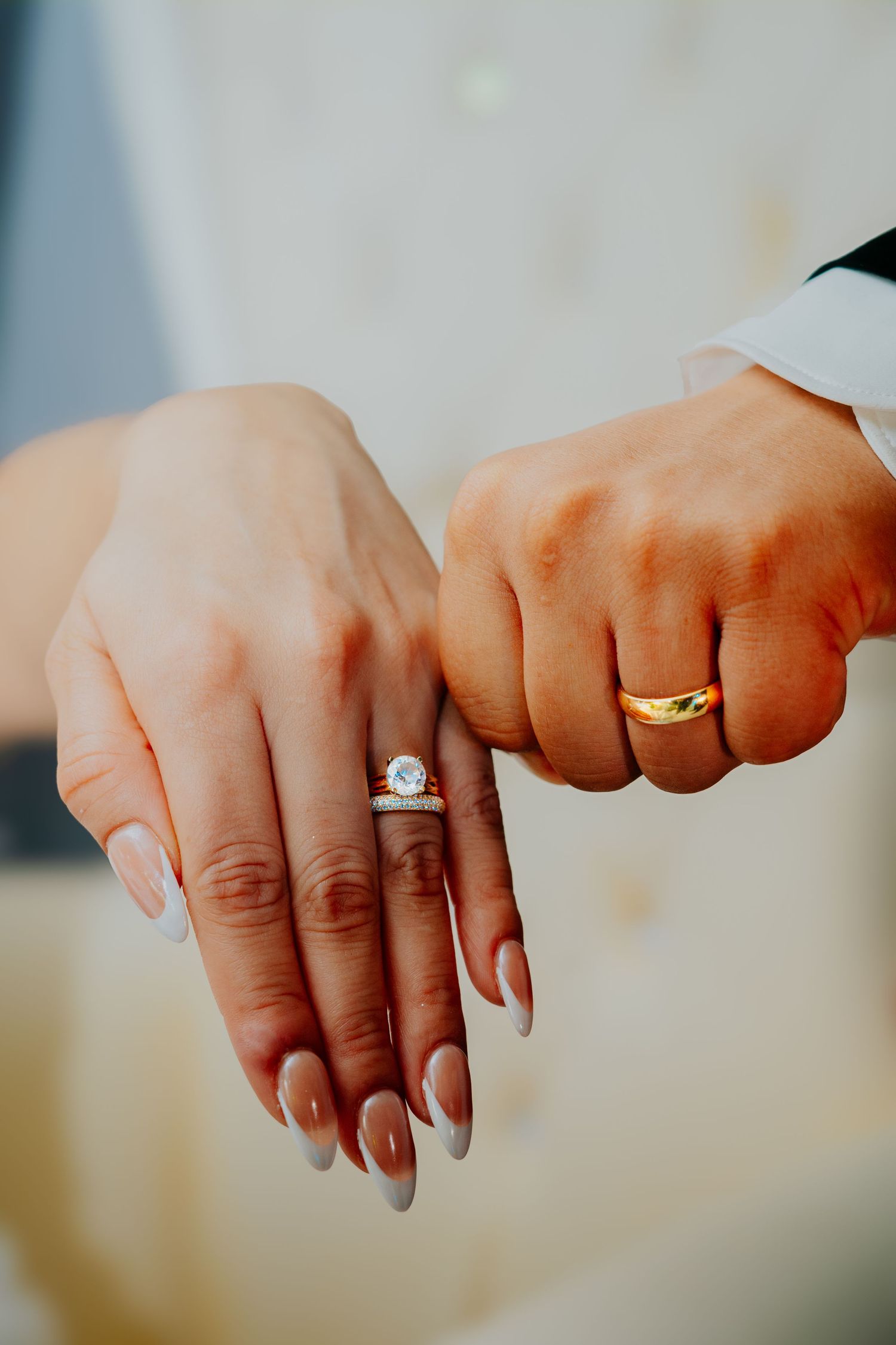 Close-up of newlyweds' hands showing their wedding rings against a soft, blurred background.
