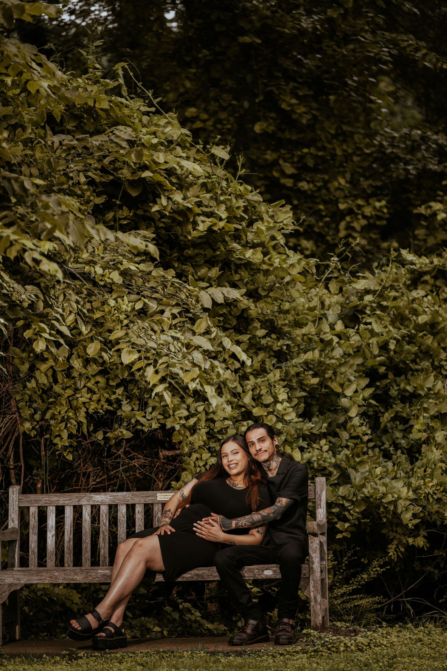 A couple relaxes together on a wooden bench surrounded by lush greenery.
