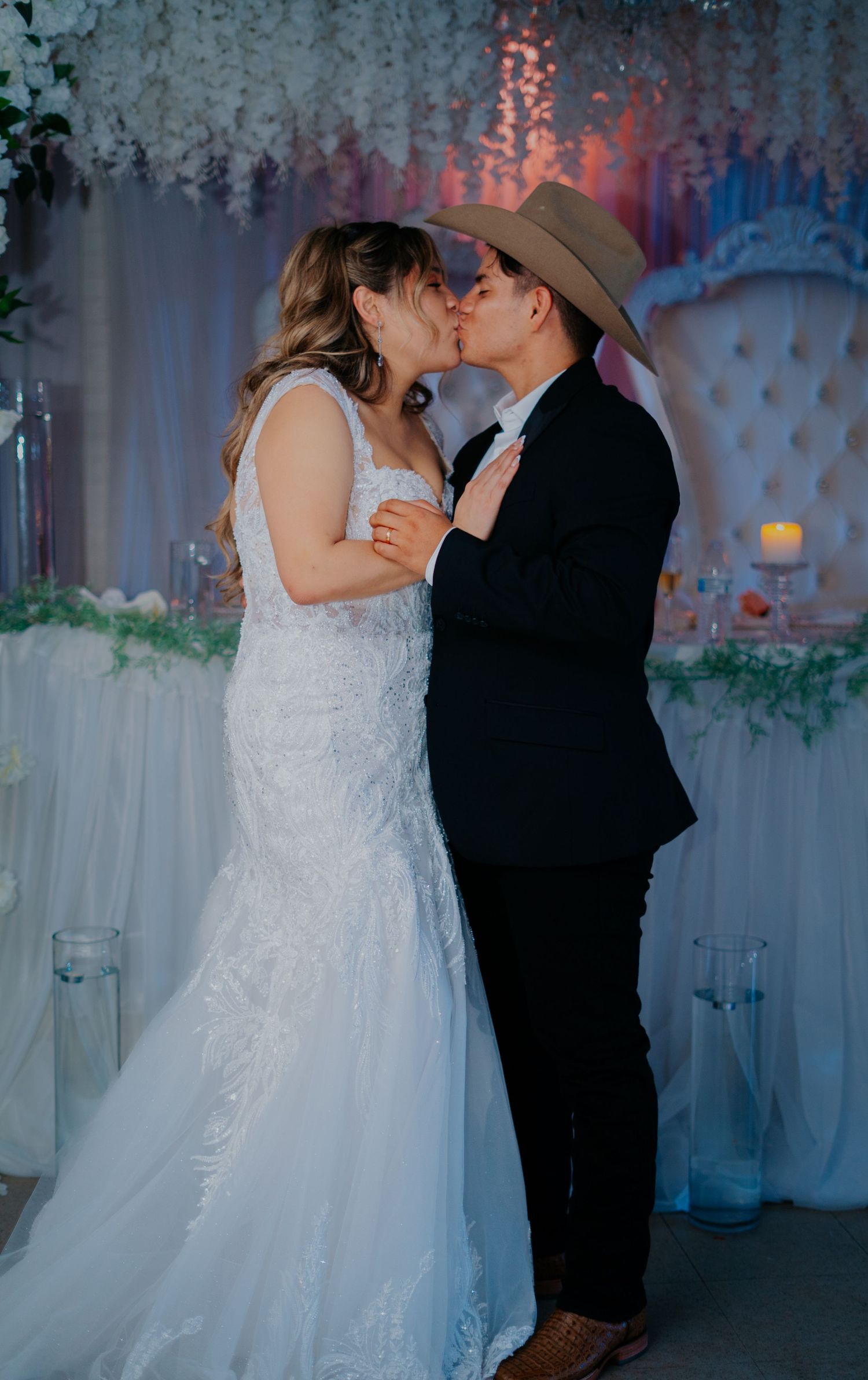 A romantic wedding couple shares an intimate kiss during their first dance in a dreamily lit reception venue.