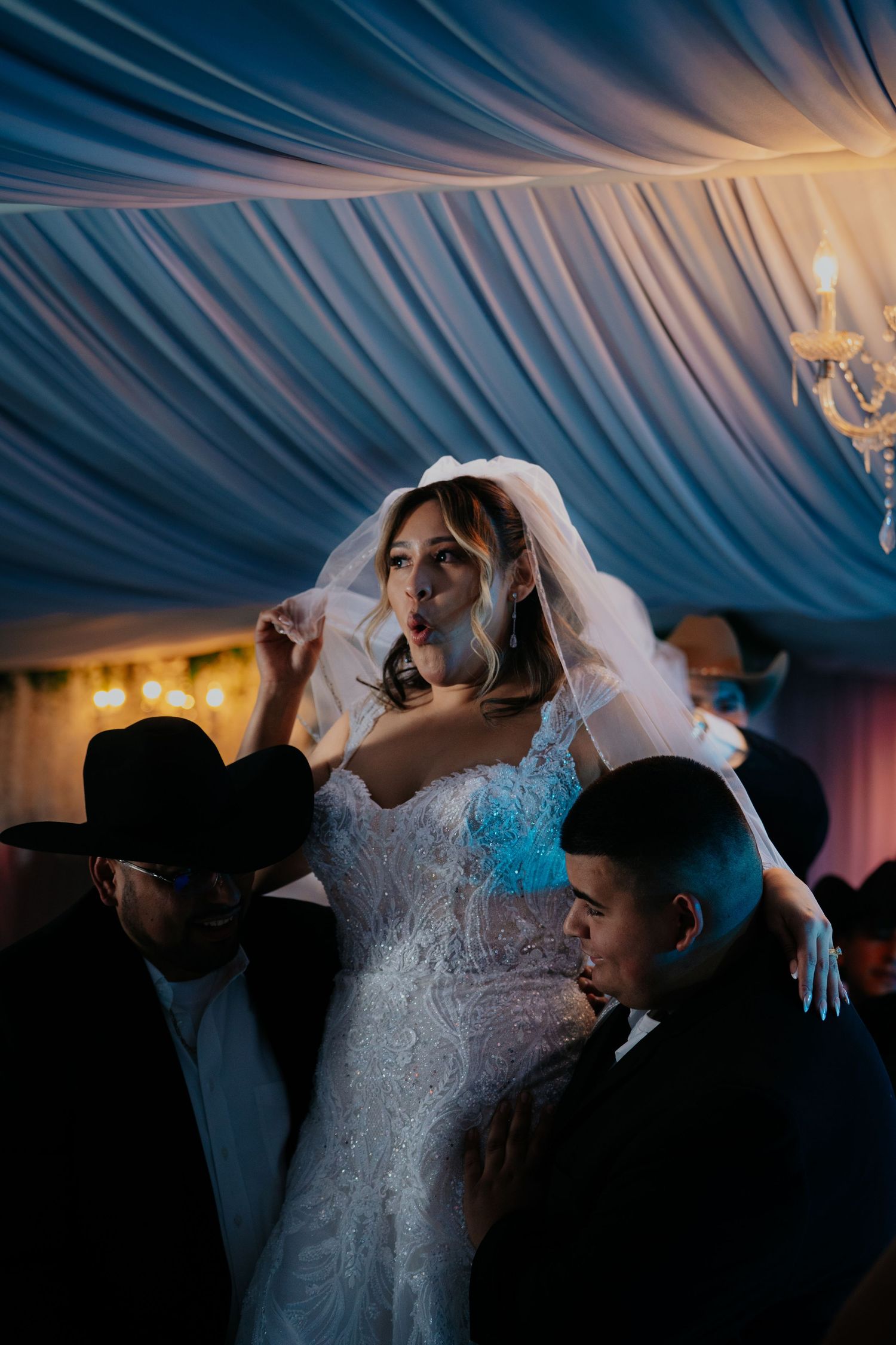 Wedding reception dance floor filled with guests celebrating under draped fabric ceiling decorations.