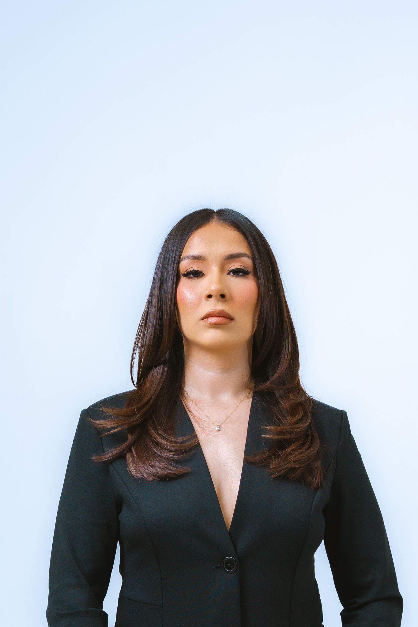 Professional portrait against light background showing person in black blazer with long dark hair and confident expression.