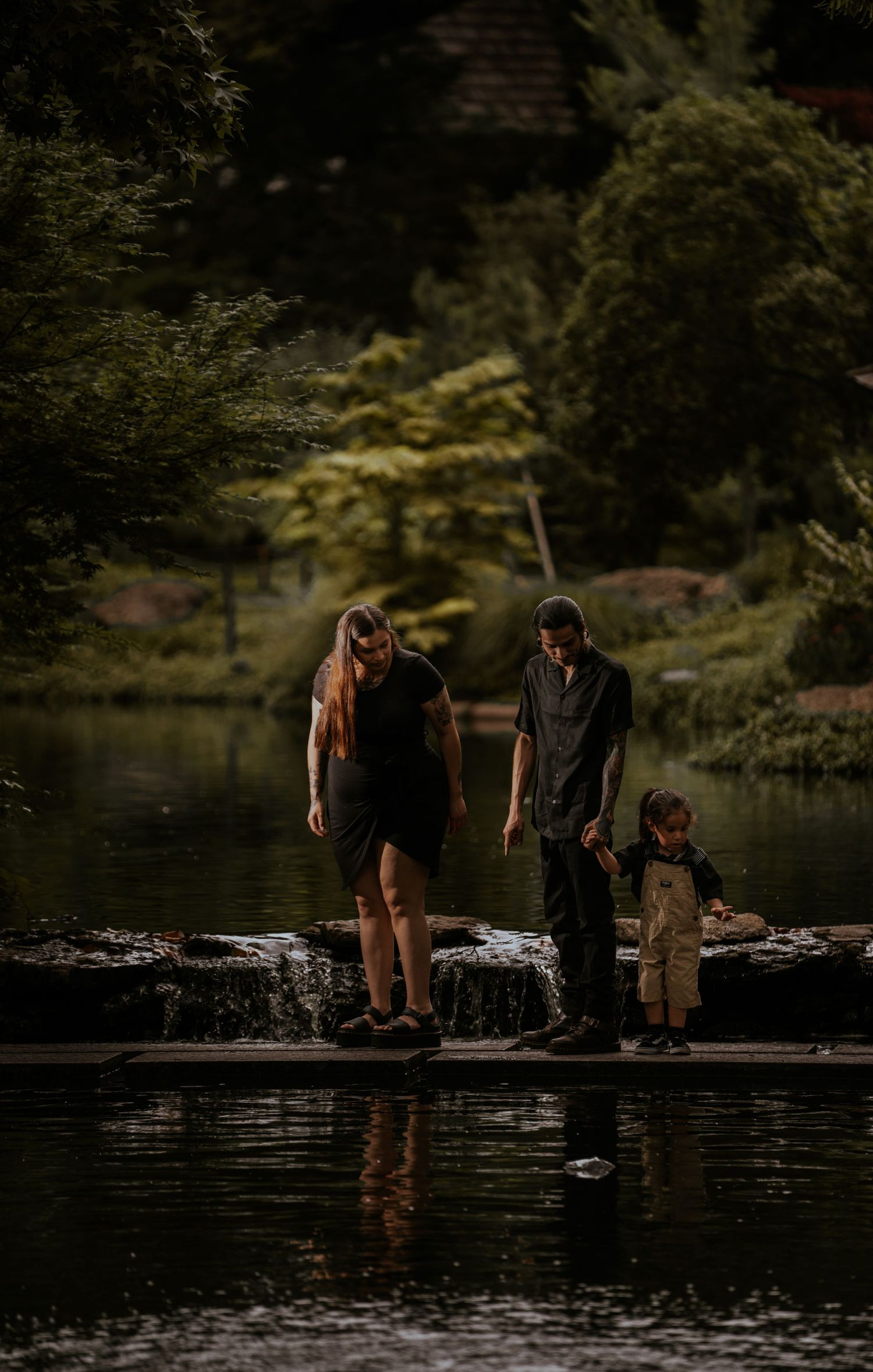 Three people explore the edge of a serene lake surrounded by lush greenery.