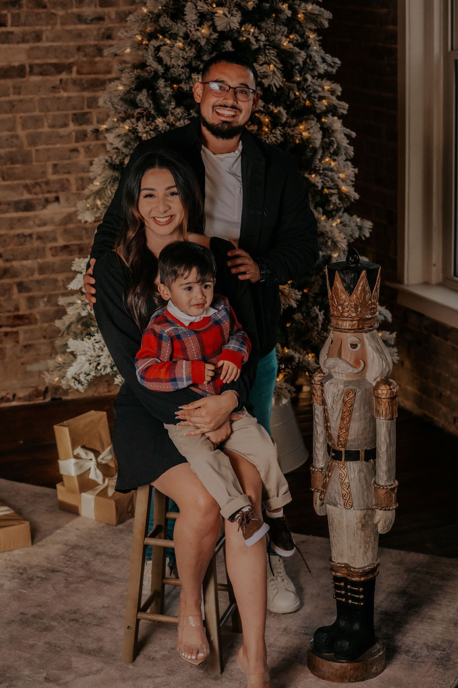 A family poses for a holiday portrait next to a decorated Christmas tree and nutcracker decoration.