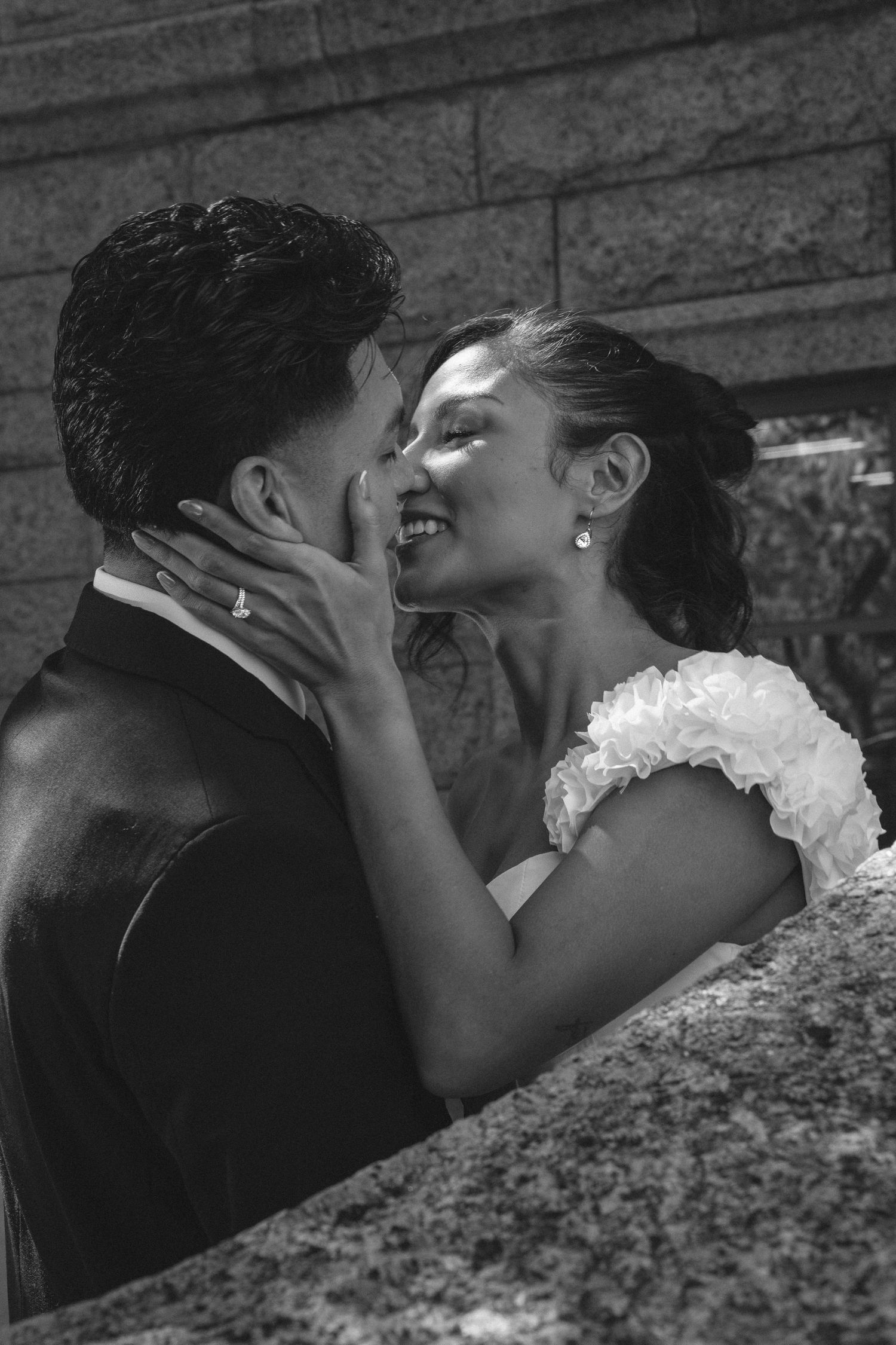 A romantic black and white photo series showing a couple sharing intimate kisses against a textured stone wall.