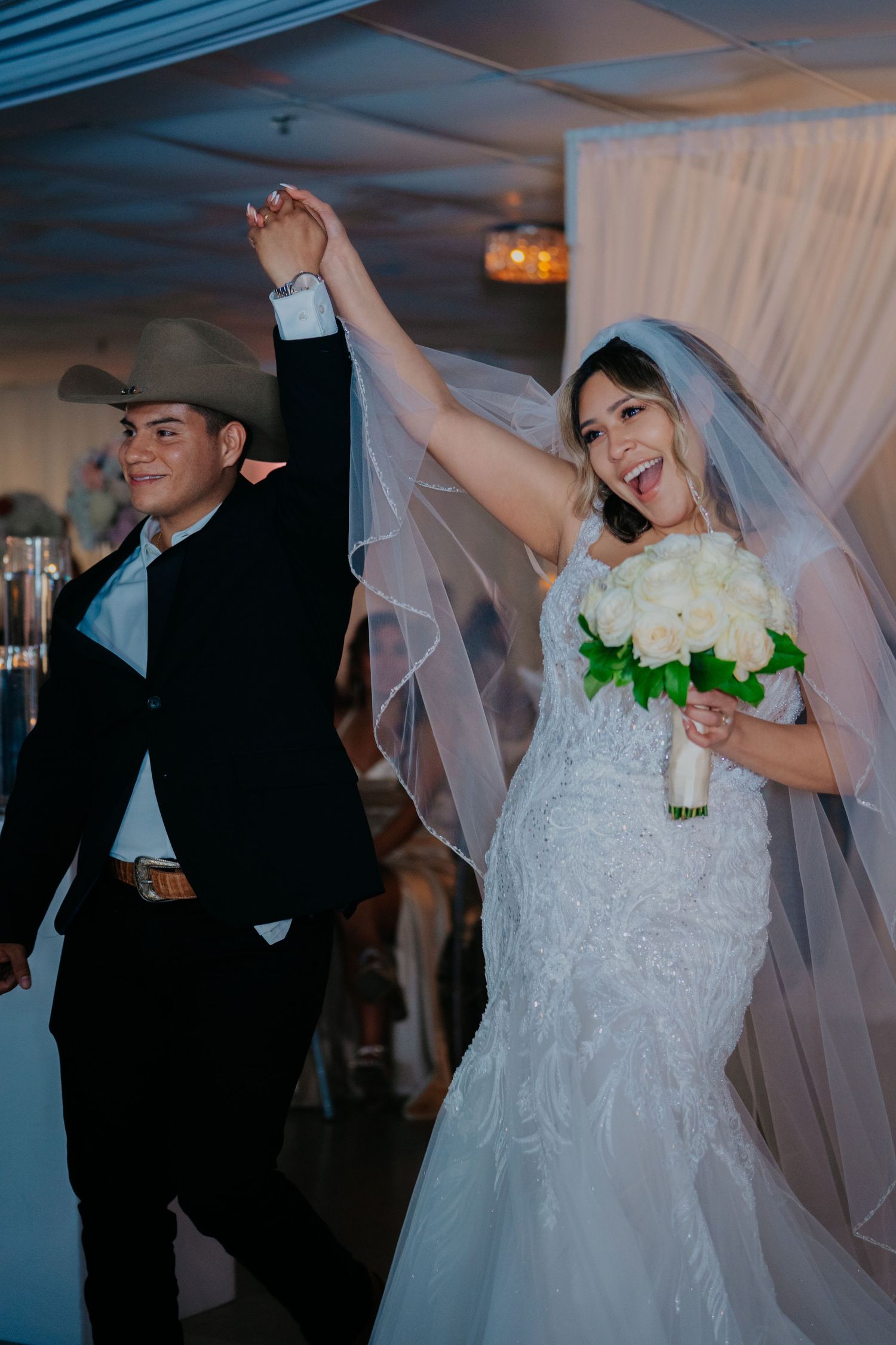 Newlyweds share a joyful dance together at their wedding reception with white decor and dim lighting.