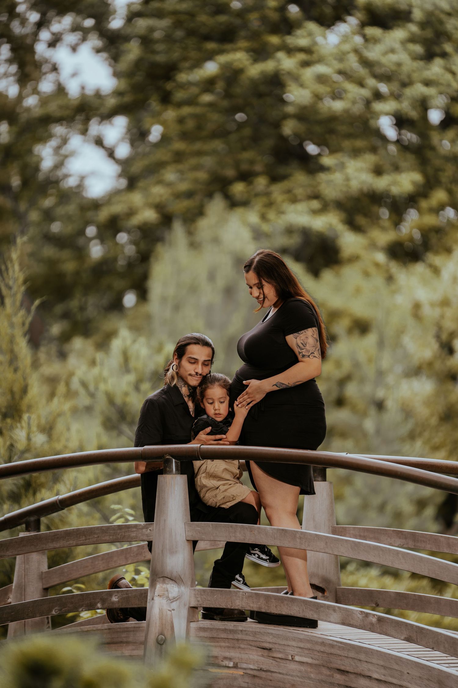 A couple shares an intimate moment on a wooden bridge in a lush garden setting.