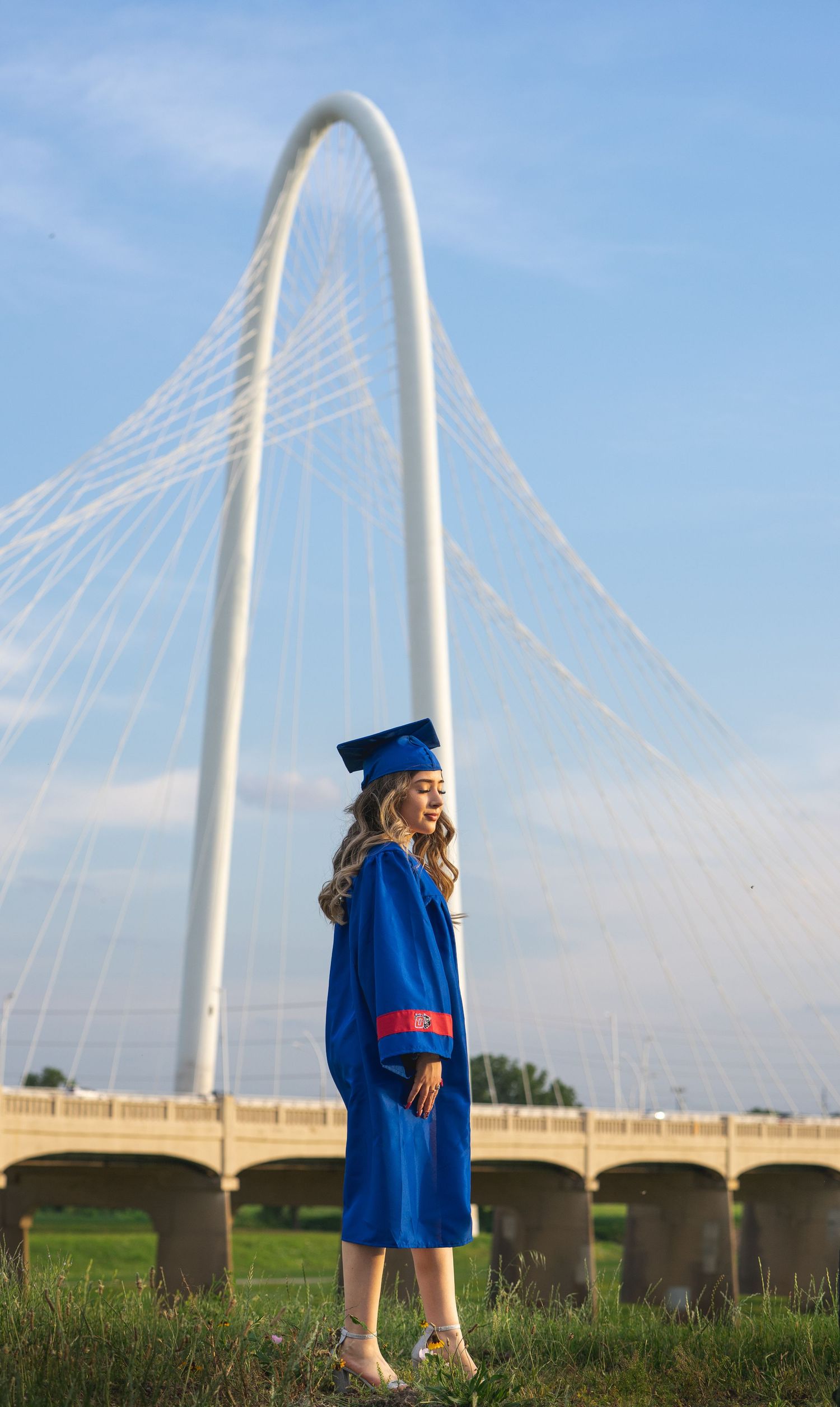 A series of graduation photos showing someone in blue cap and gown posing near a modern white bridge structure.
