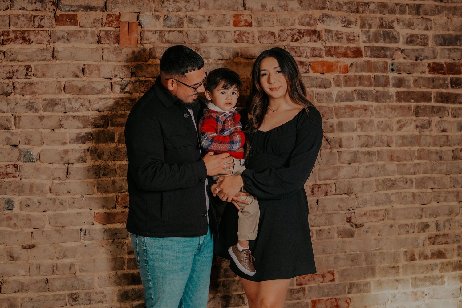 A family shares joyful moments together against a rustic brick wall backdrop in a lifestyle photography session.