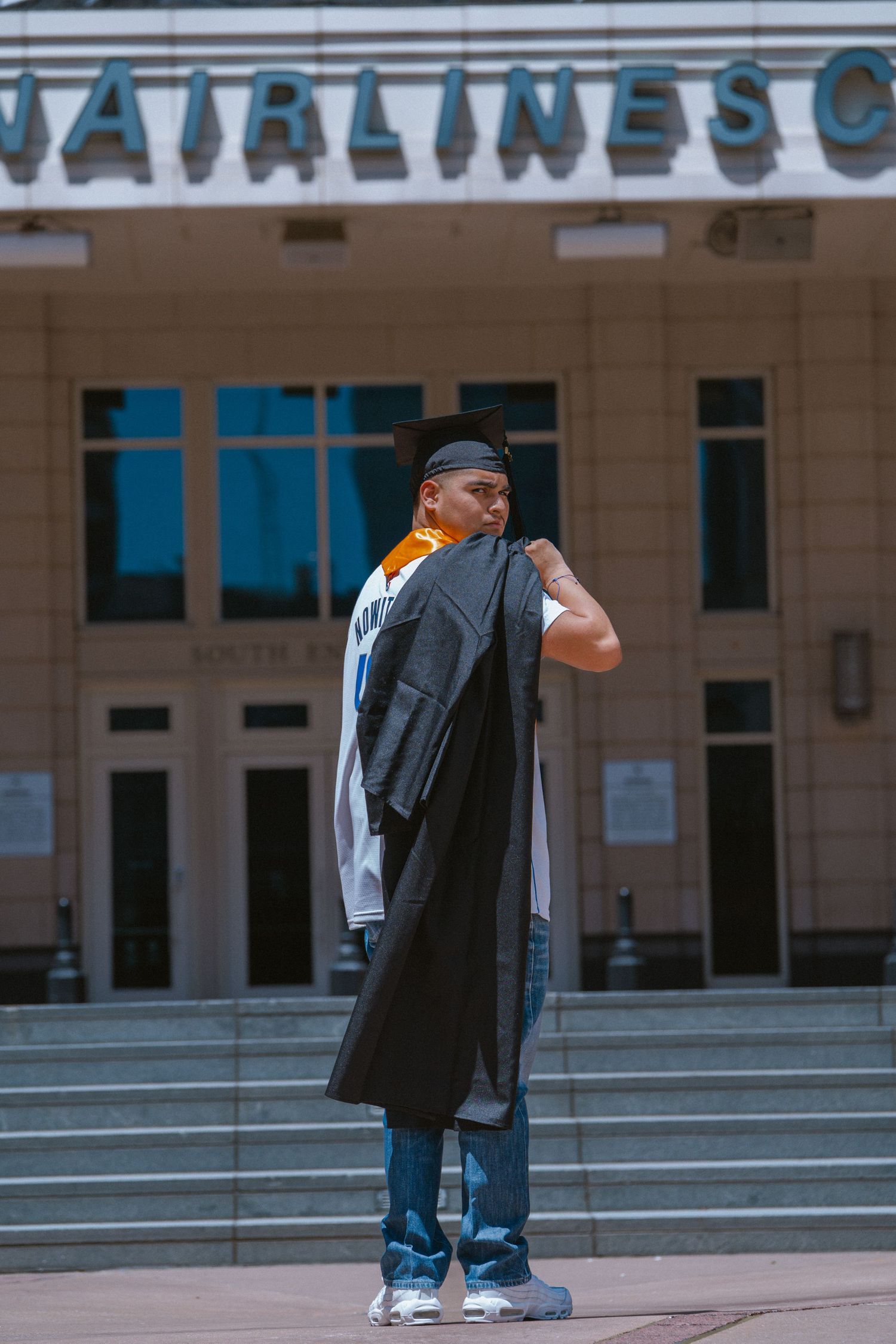 Graduate in cap and gown standing before American Airlines Center in Dallas Texas.