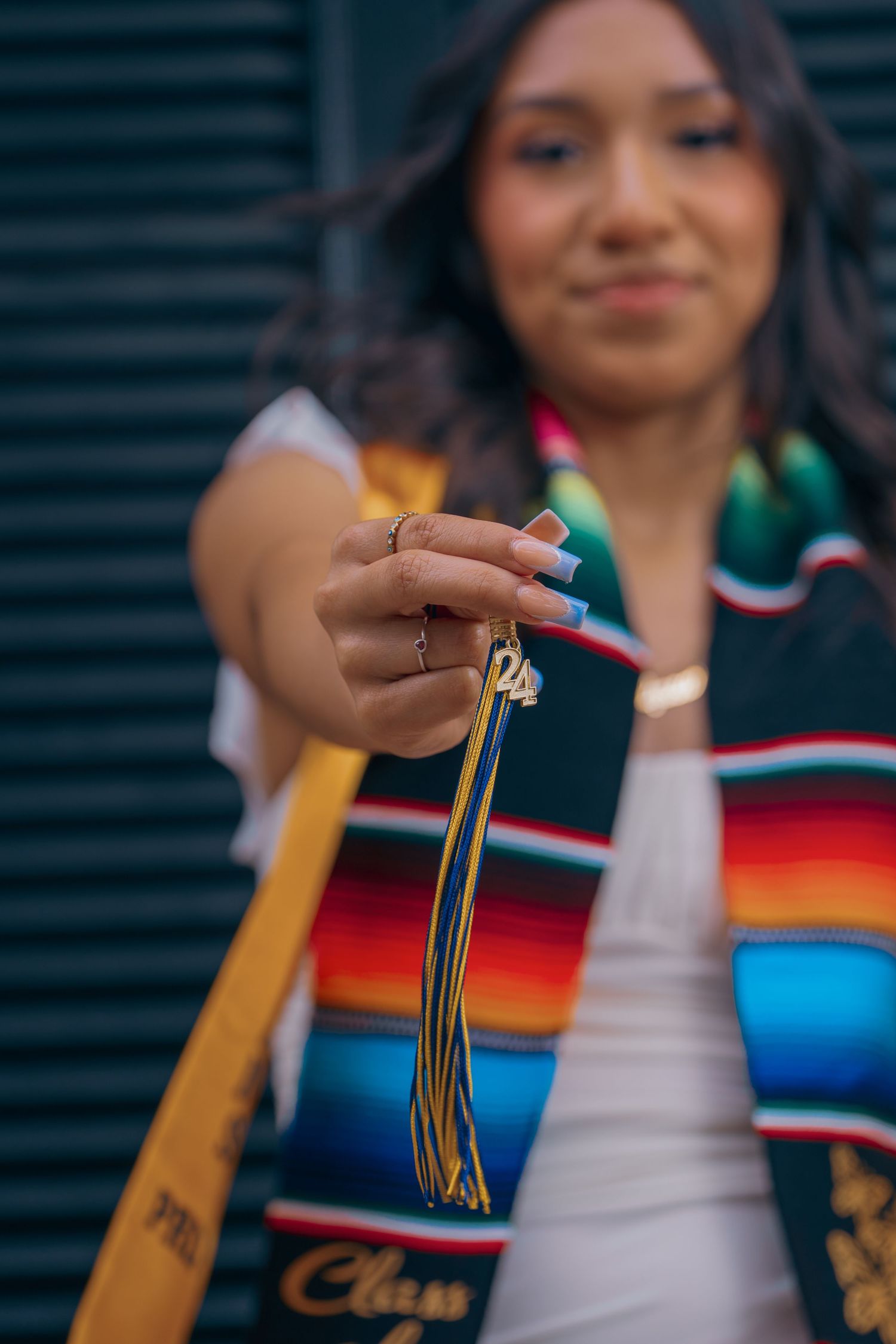 Close-up of graduation tassel and colorful serape stole against dark background.