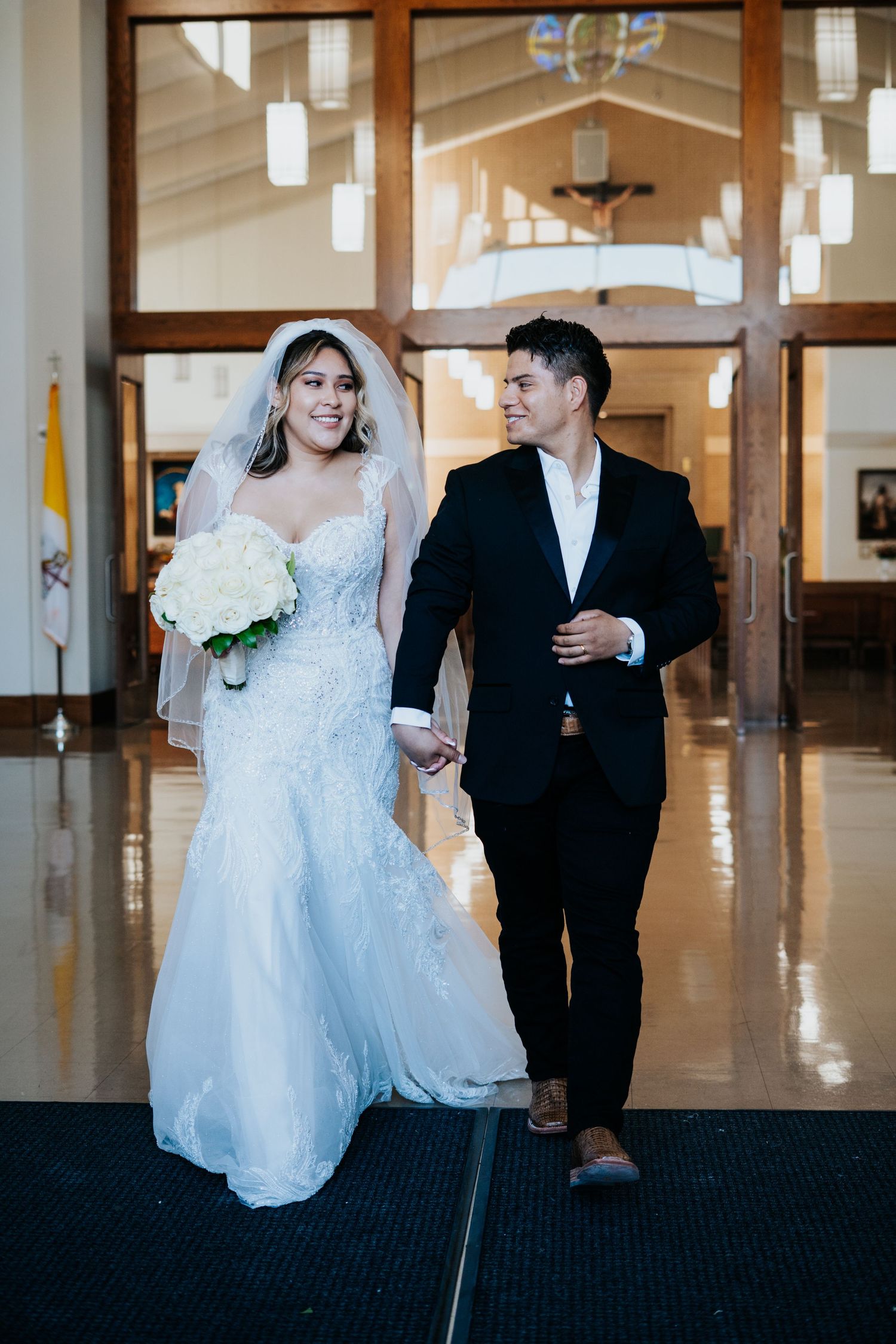 Wedding couple stands together in an elegant hall with polished floors and modern lighting fixtures.