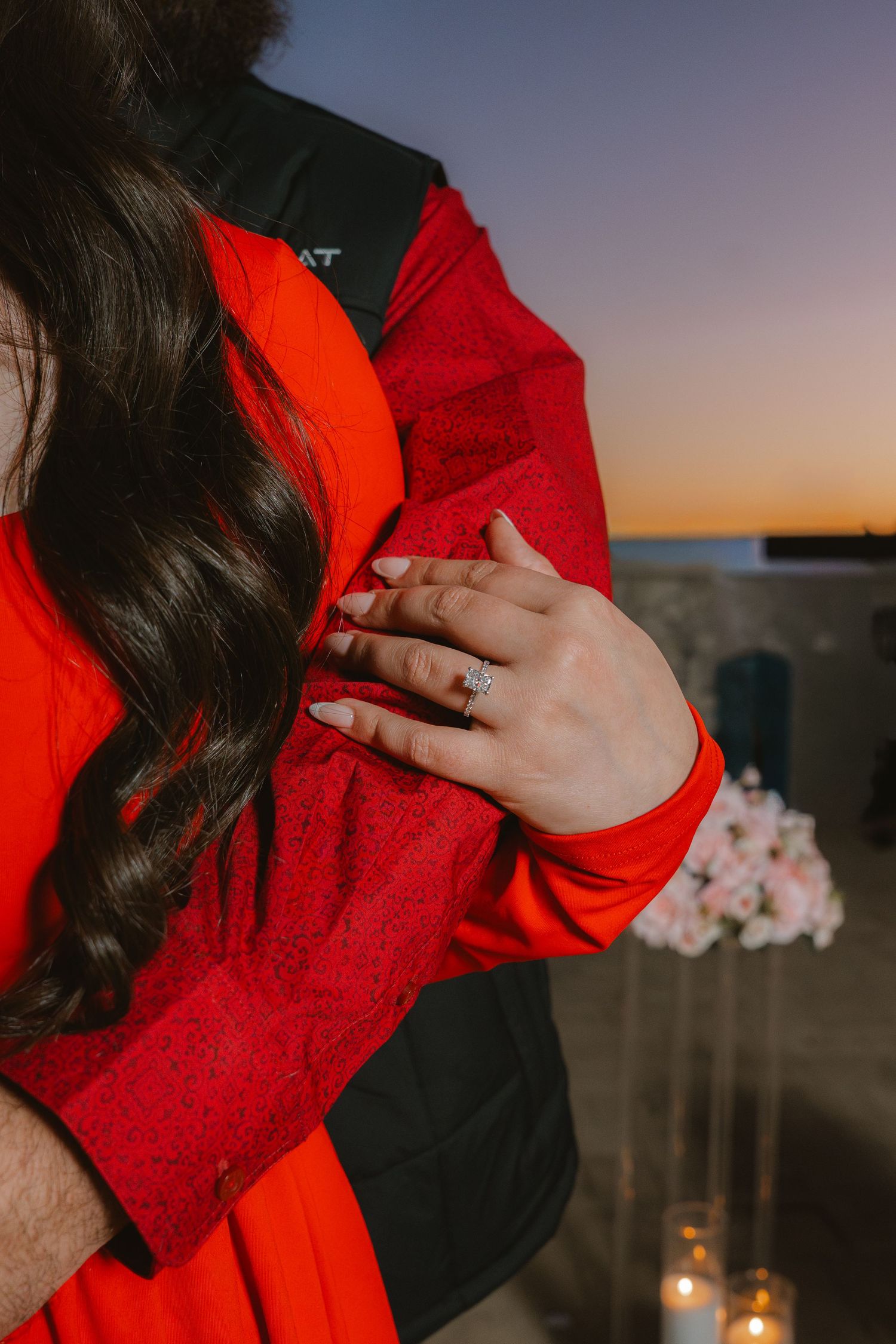 Close-up of a woman's hand displaying a diamond engagement ring while embracing her partner at sunset.